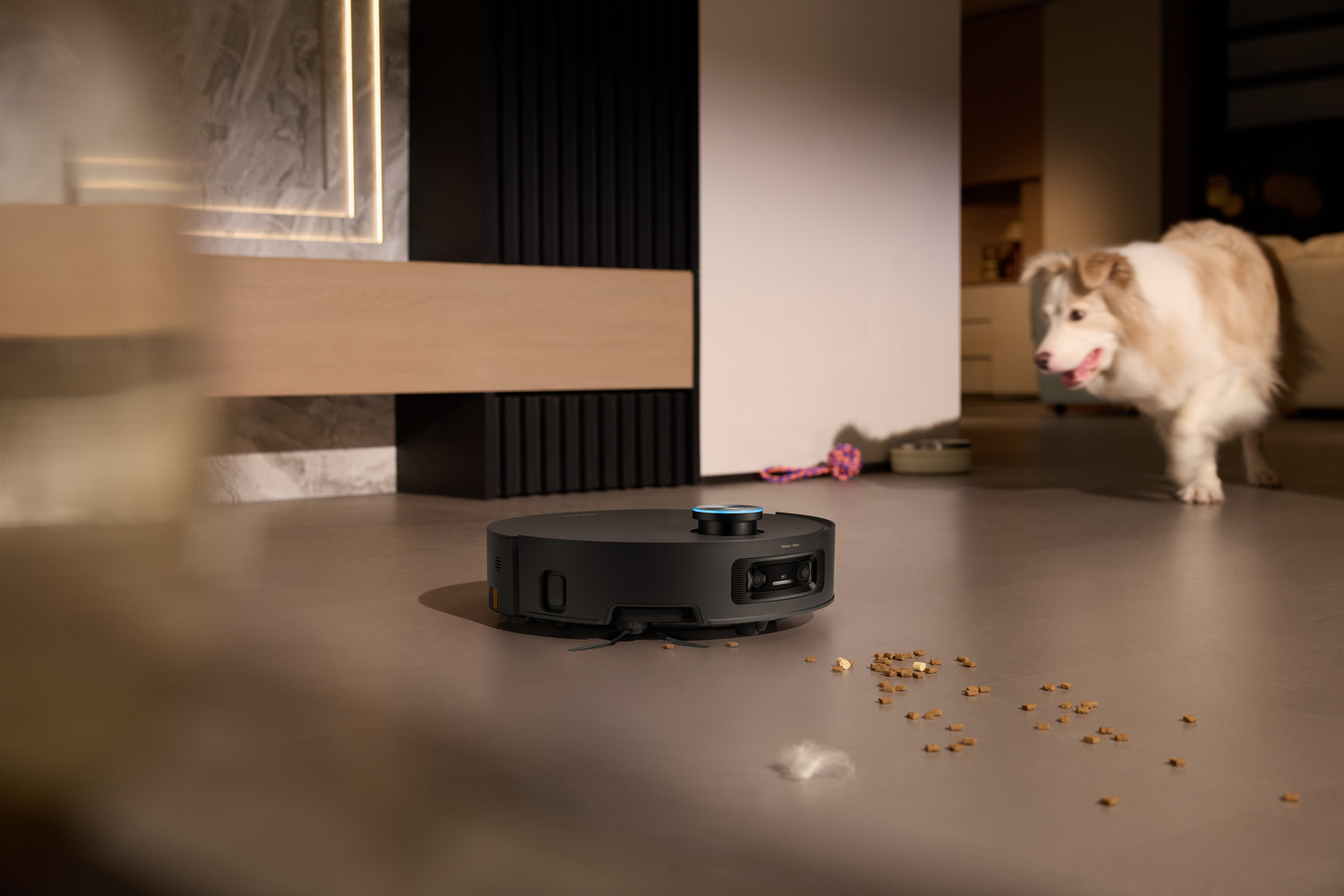 Una aspiradora robot en el suelo con comida y pelo de perro. Un perro camina al fondo.