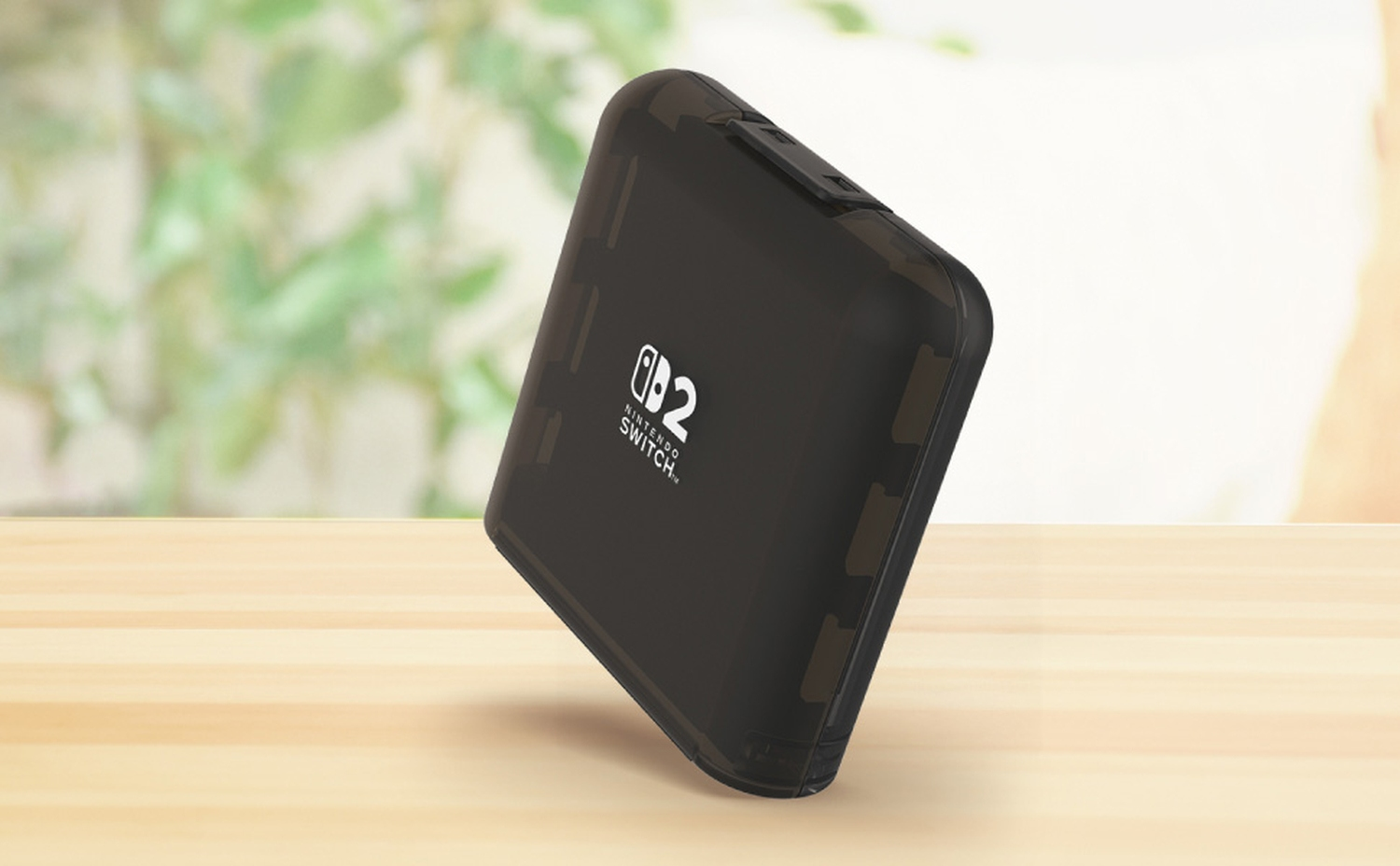 Una custodia nera per Nintendo Switch su un tavolo di legno. Lo sfondo è sfocato con tonalità verdi e bianche.
