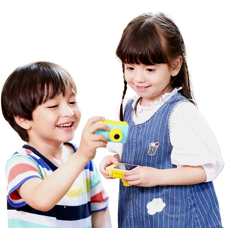 Deux enfants souriants tiennent des appareils photo. Garçon en chemise rayée, fille en robe en jean. Appareils photo jaunes et bleus. Fond blanc.