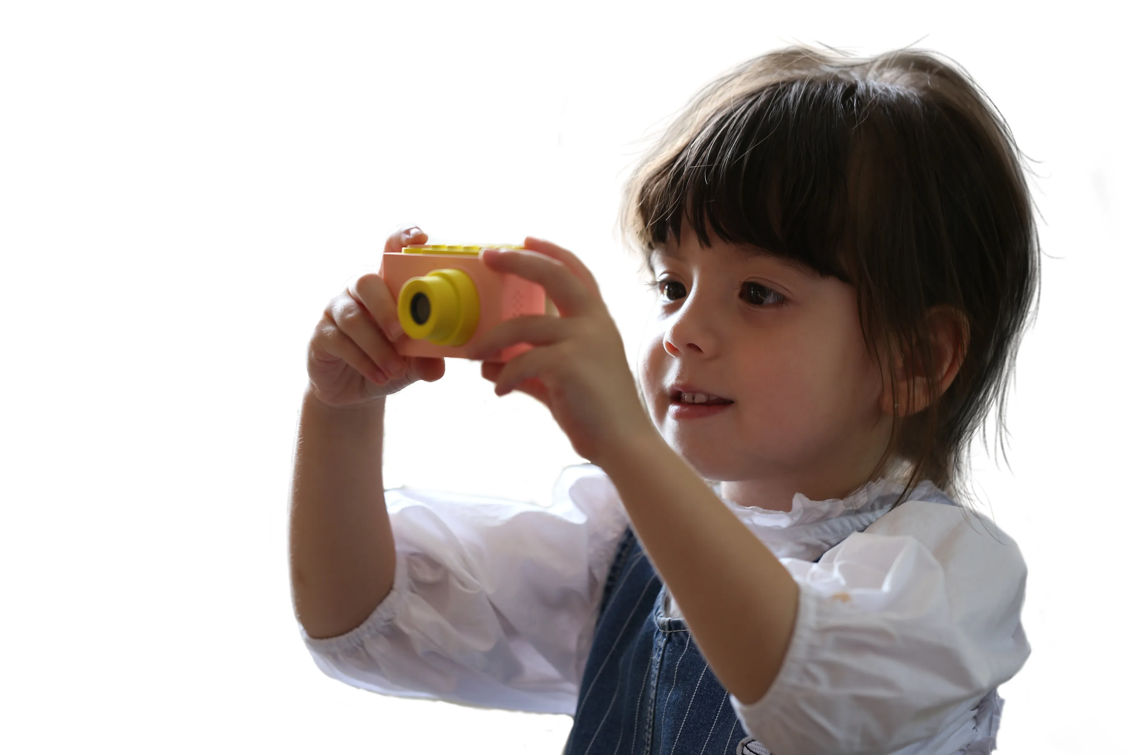 Un jeune enfant tenant un appareil photo jouet rose. L'enfant sourit et regarde l'appareil.