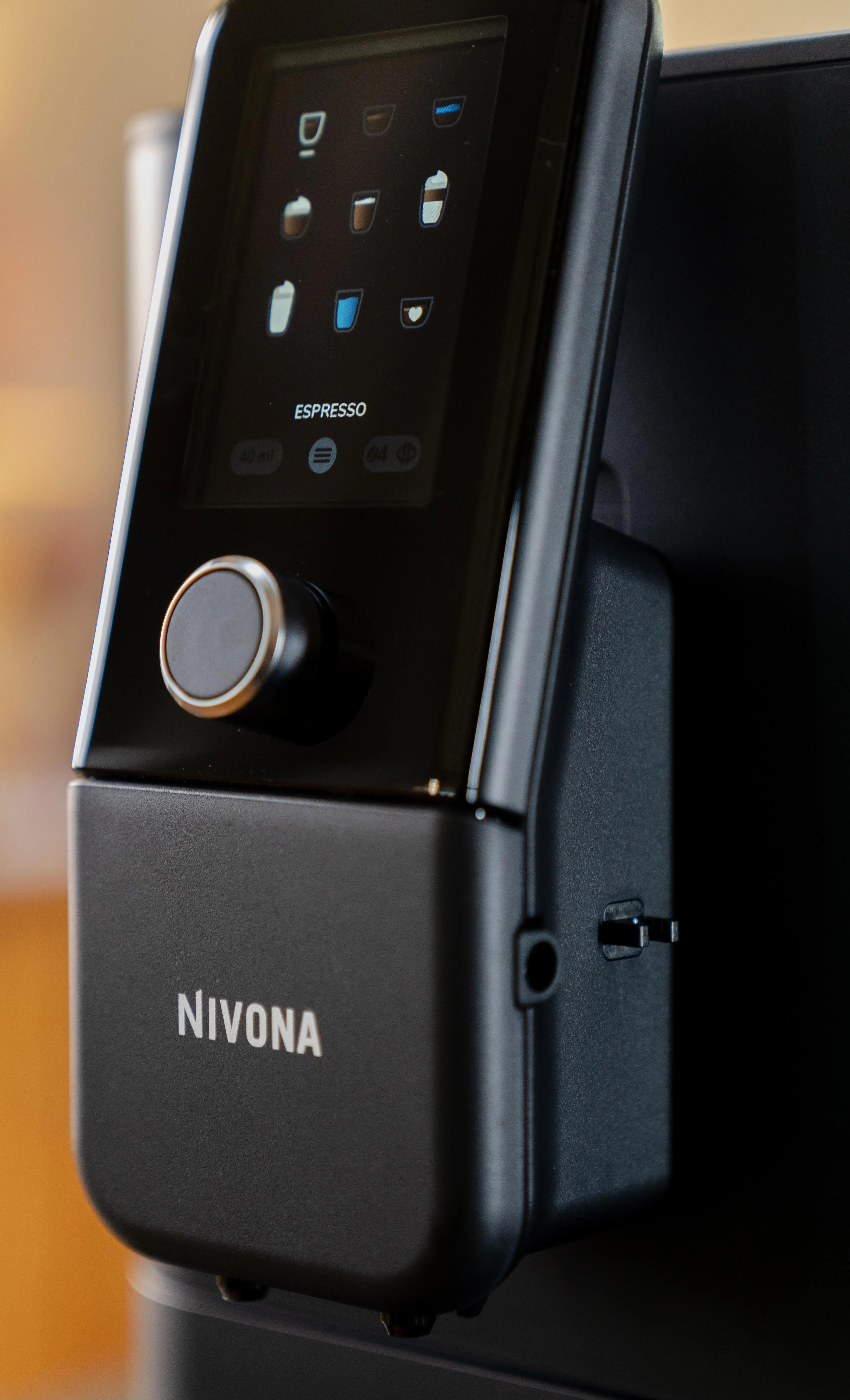 Zbliżenie czarnego ekspresu do kawy Nivona z wyświetlaczem pokazującym opcje kawy i pokrętłem sterowania. Tło jest rozmyte.