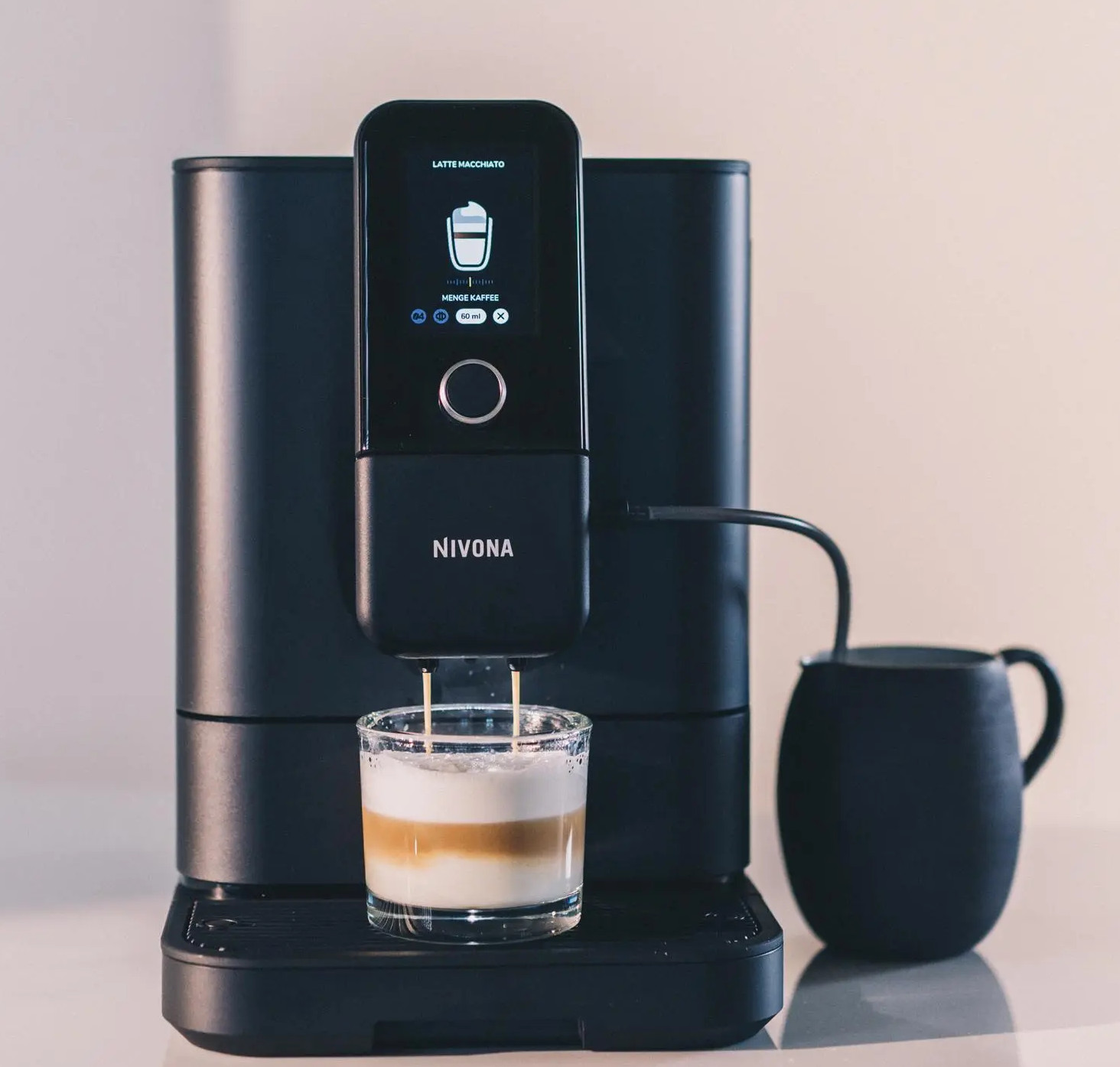 Czarny ekspres do kawy Nivona robi latte macchiato. Kawa wlewa się do szklanki, obok czarnego kubka.