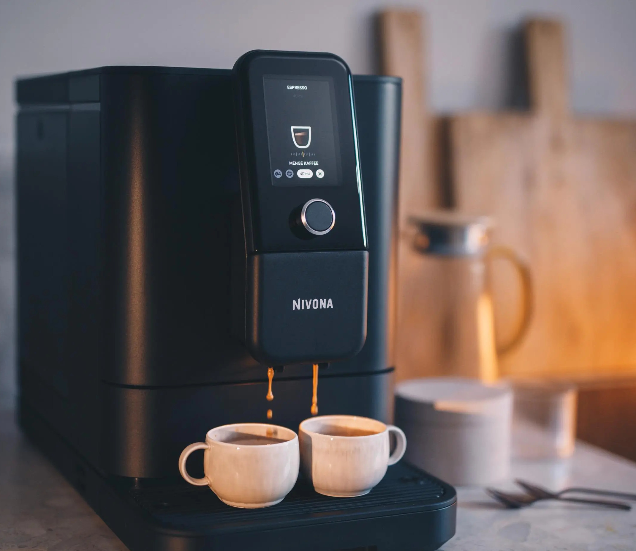 Czarny ekspres do kawy nalewa kawę do dwóch białych filiżanek. Tło przedstawia drewniane deski i słoik.