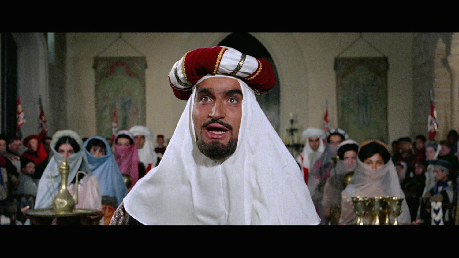 Ein Mann in weißem Gewand und Turban blickt überrascht, umgeben von Menschen in mittelalterlicher Kleidung. Die Szene spielt in einer Kirche.