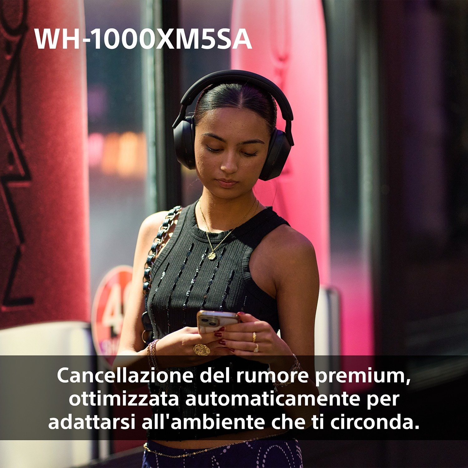 Una donna con le cuffie guarda il telefono. Si trova in un ambiente urbano. Il testo dice cancellazione del rumore premium.