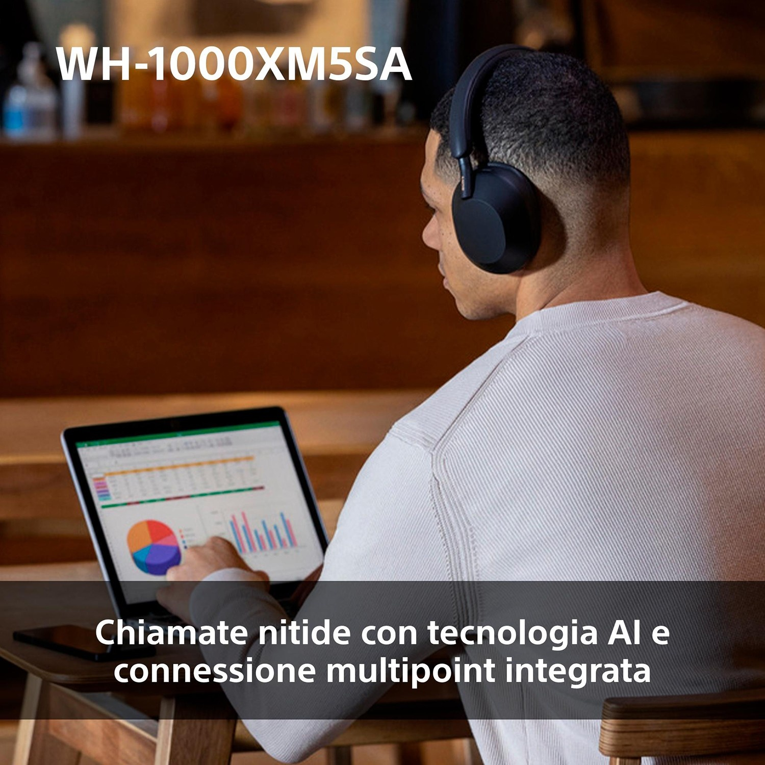 Un uomo con le cuffie lavora su un laptop con grafici. È seduto a un tavolo di legno. Testo in basso nell'immagine.