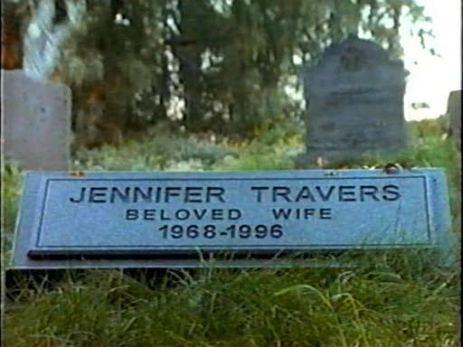 Ein Grabstein mit der Aufschrift 'Jennifer Travers, geliebte Ehefrau, 1968-1996'. Die Szene ist ein Friedhof mit Grün und anderen Grabsteinen.