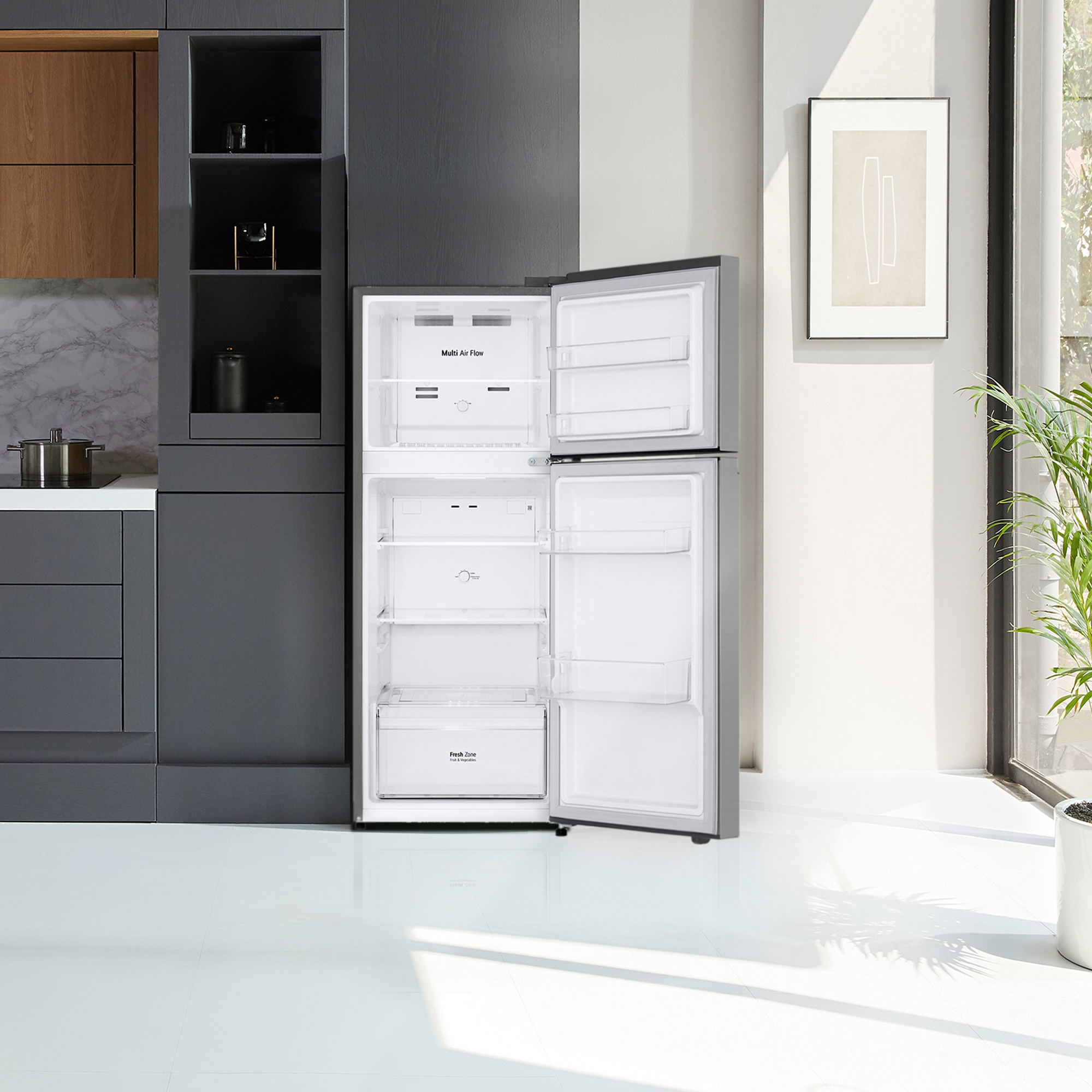Refrigerador abierto en cocina moderna. Interior blanco, exterior acero inoxidable. Plantas, arte enmarcado, gabinetes.
