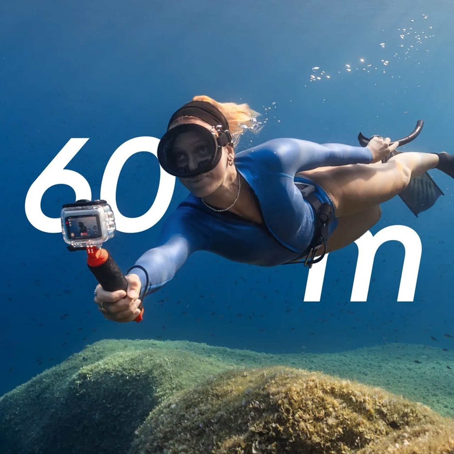 Una donna si immerge sott'acqua con una telecamera, con una muta e una maschera. Grande testo '60 m' sovrapposto.