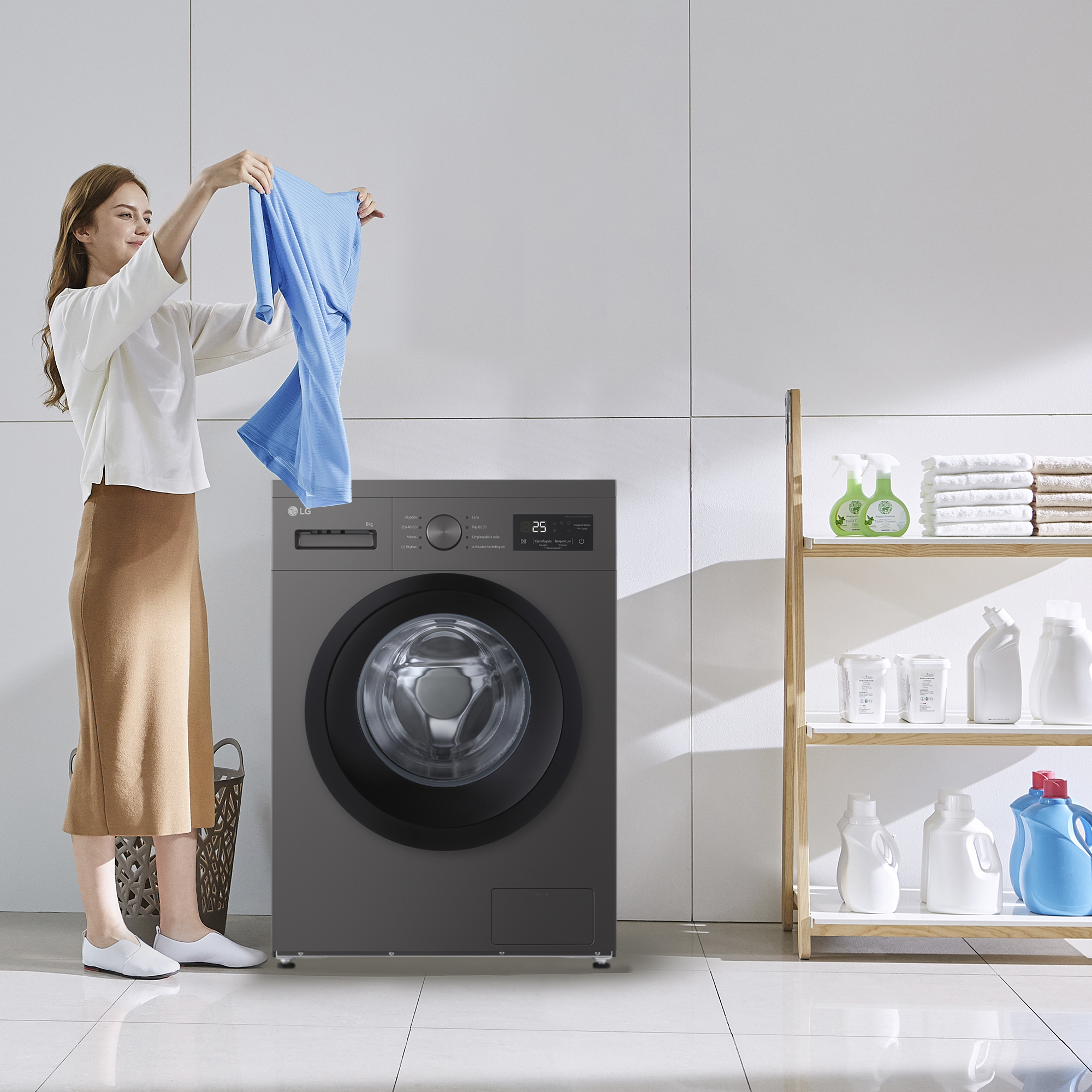 Mujer sosteniendo camisa azul frente a lavadora. Lavadero con estantes de productos de limpieza.