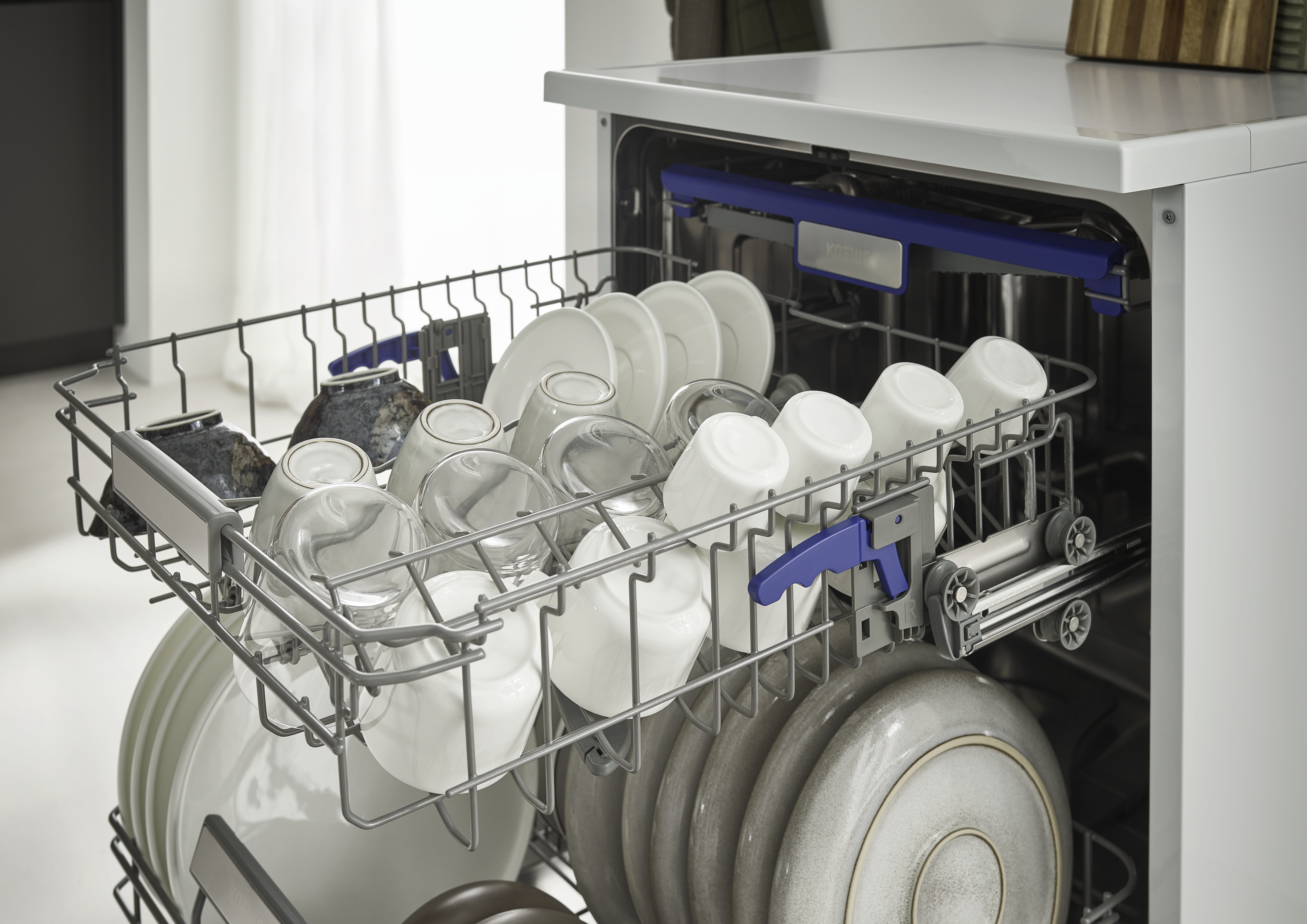 Geschirrspüler gefüllt mit weißen Tassen, Tellern und Gläsern. Blaue und graue Akzente auf dem Geschirrspüler. Küchenumgebung.