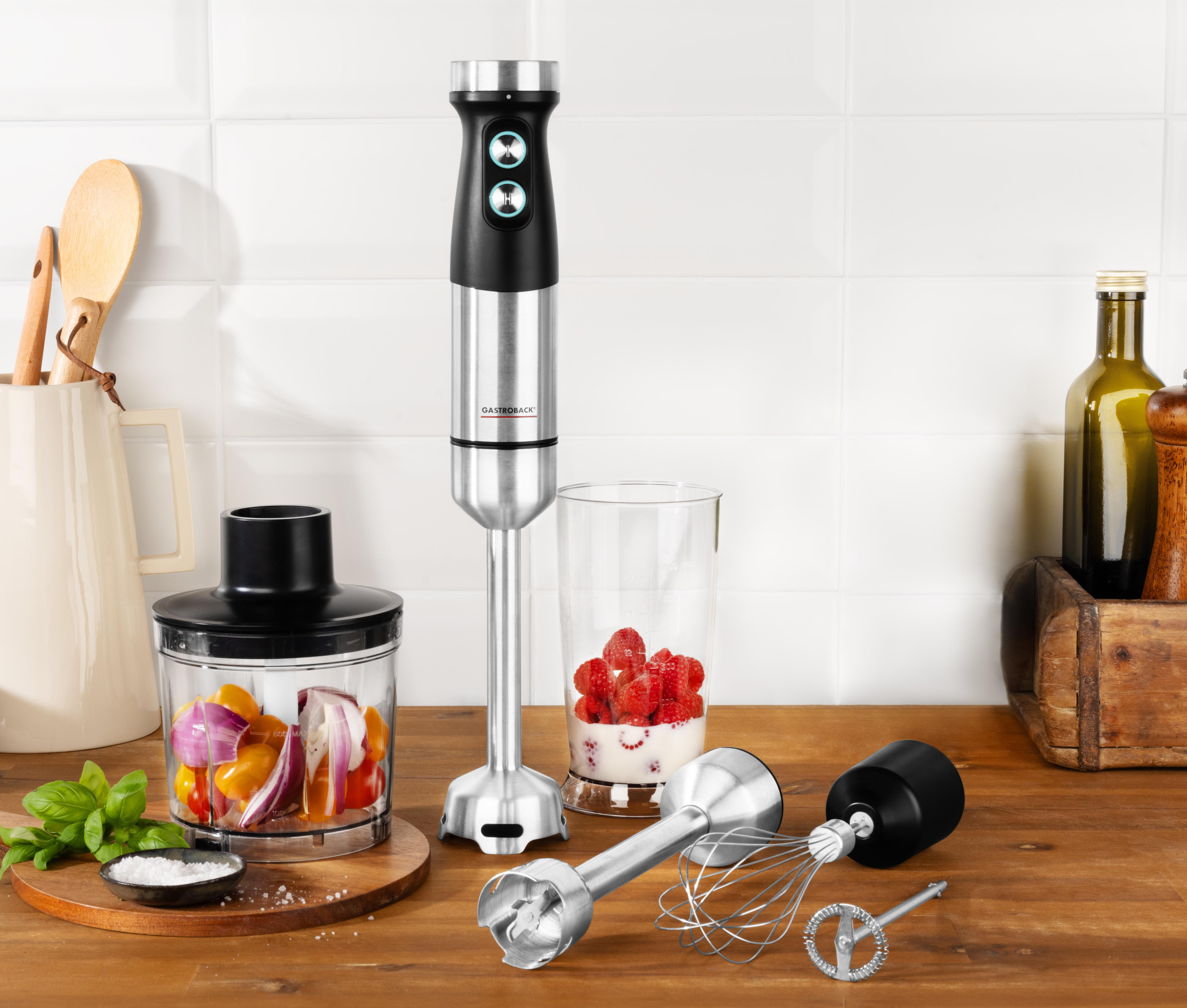 Eine Küchenszene mit einem Mixer, Zutaten und Zubehör auf einer Holzoberfläche. Weiße Fliesenwand im Hintergrund.