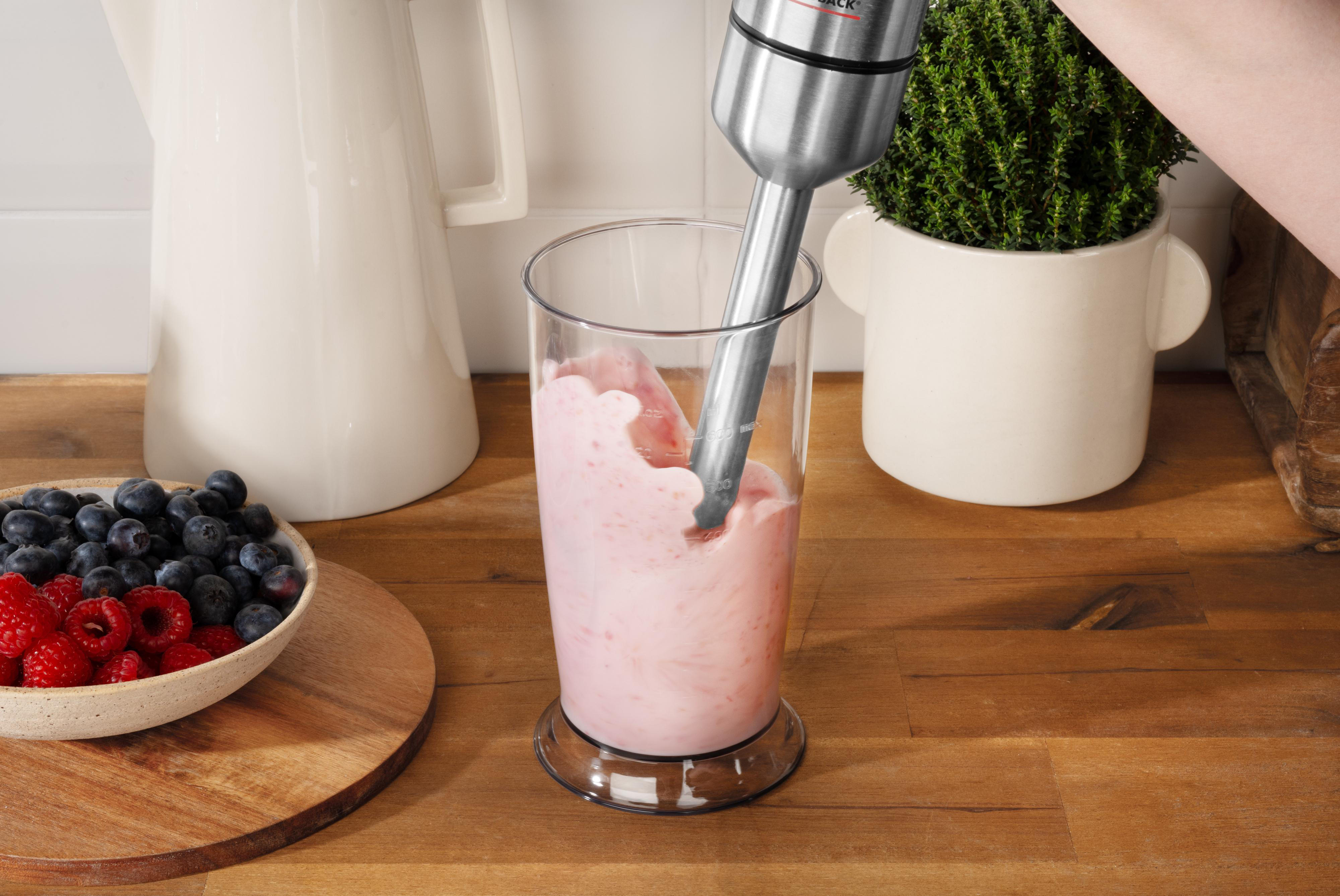 Ein Mixer mischt rosa Flüssigkeit in einem Glas. Beeren sind in einer Schüssel neben dem Glas. Eine Pflanze ist im Hintergrund.