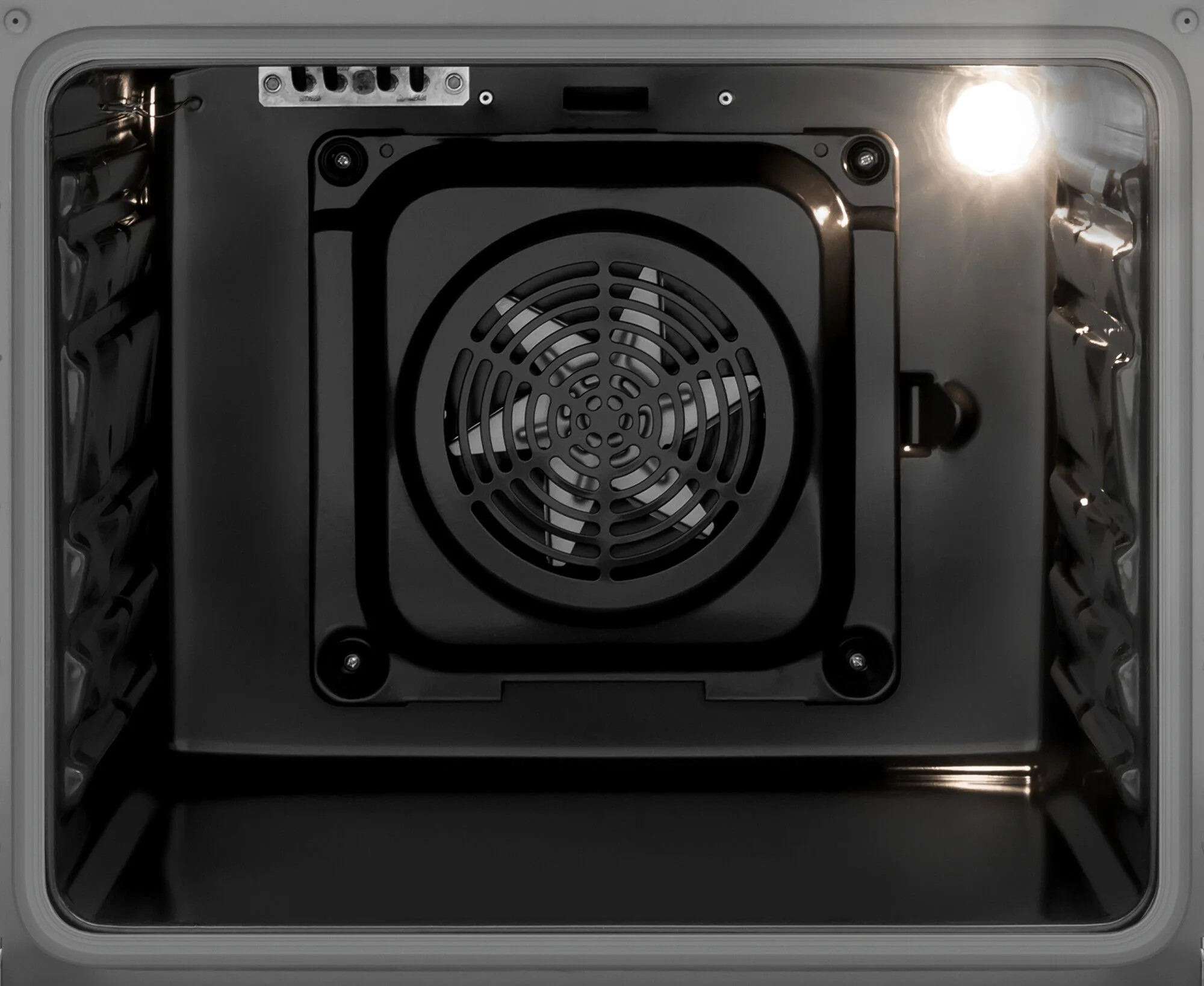 Wnętrze piekarnika. Wentylator pośrodku. Światło piekarnika jest włączone. Ściany piekarnika są czarne.