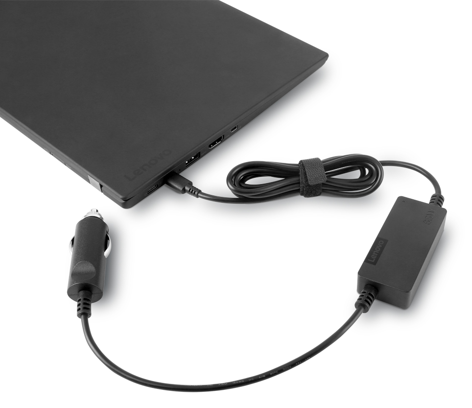 Fekete Lenovo laptop töltővel csatlakoztatva. Autós adapter is csatlakoztatva. A töltő és az adapter fehér felületen van.