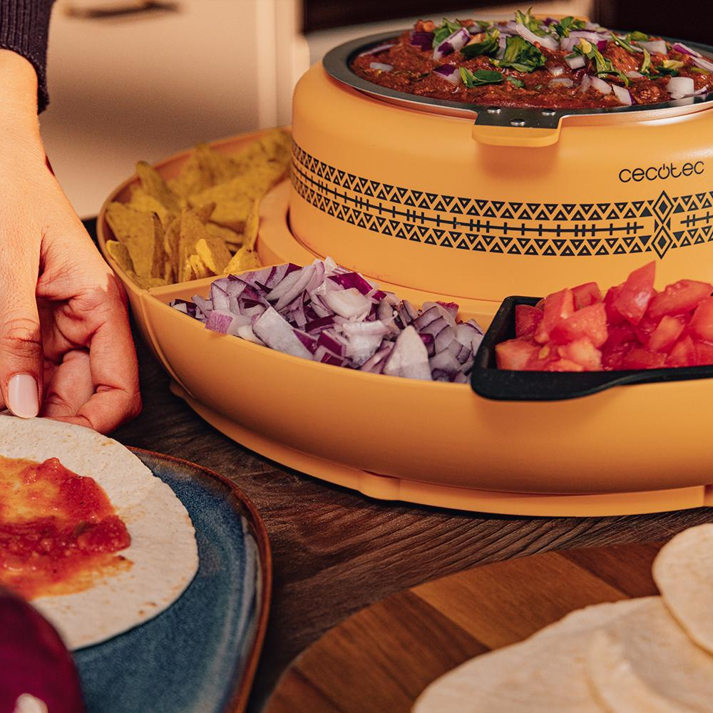 Una persona preparando una comida con un calientaplatos amarillo, tortillas, salsa, cebollas, tomates y totopos.