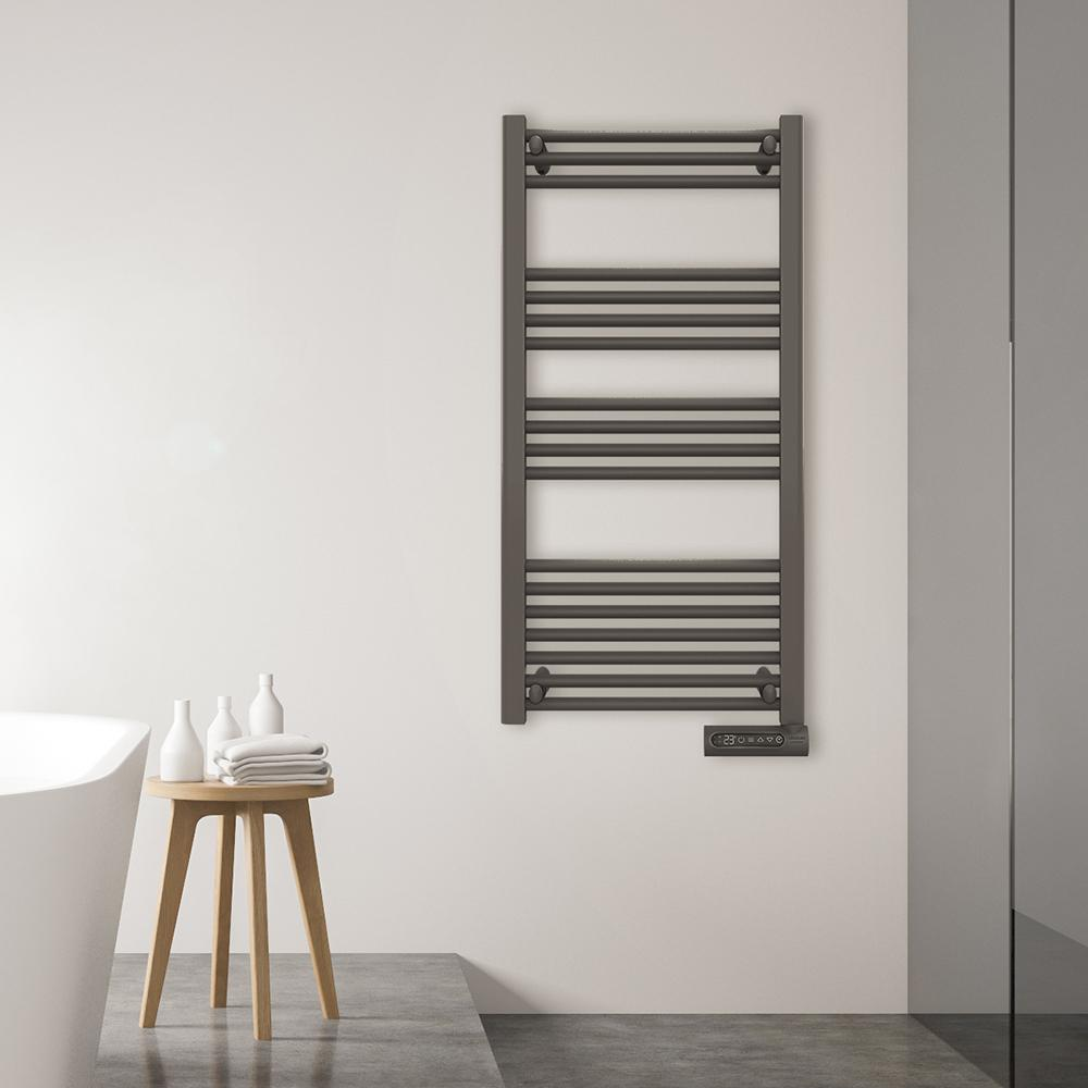Un calientatoallas gris cuelga en una pared blanca. Debajo, una mesita de madera con toallas y botellas. A la izquierda, una bañera blanca.