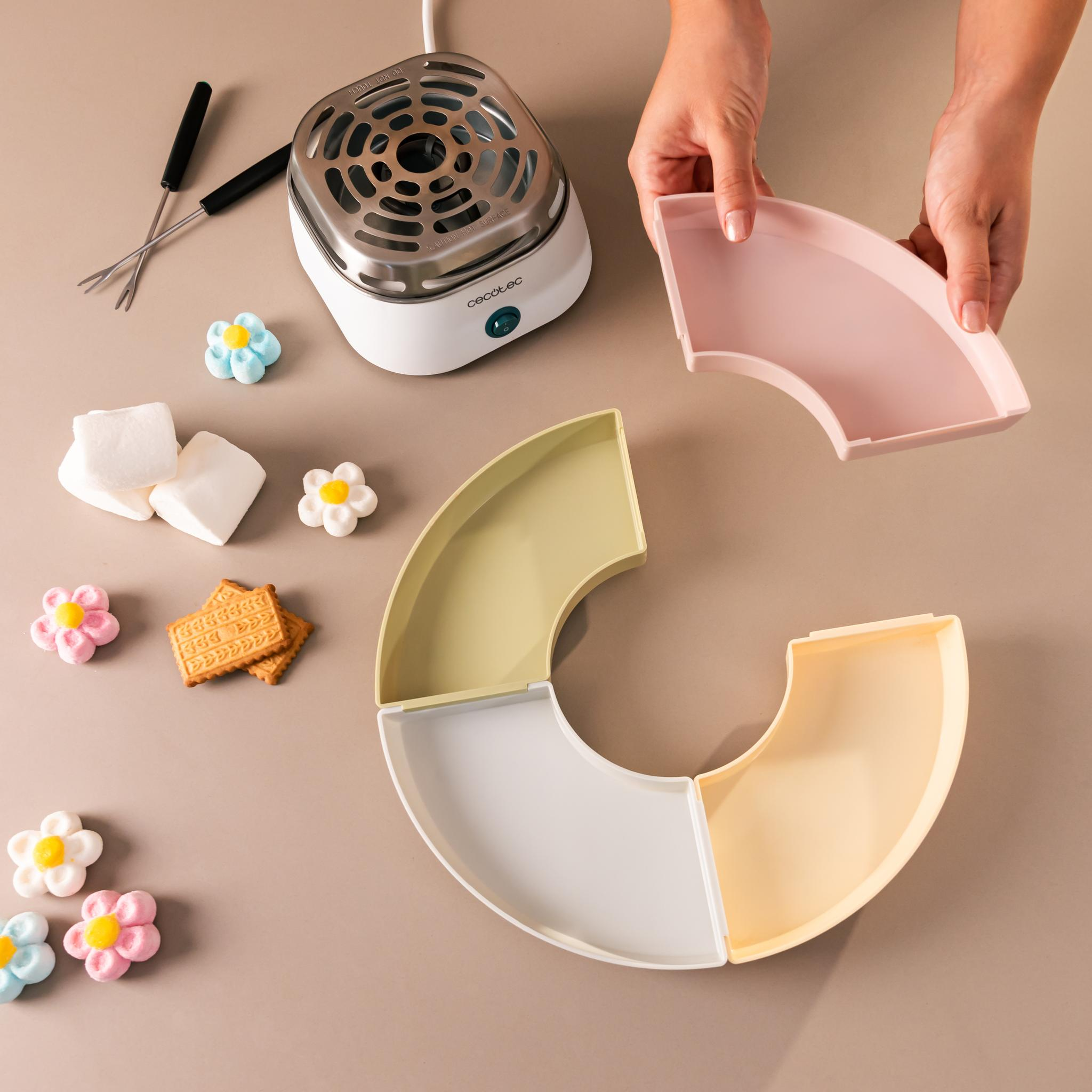 Un juego de fondue con platos, malvaviscos, galletas y caramelos en forma de flor. Manos sostienen un plato rosa.