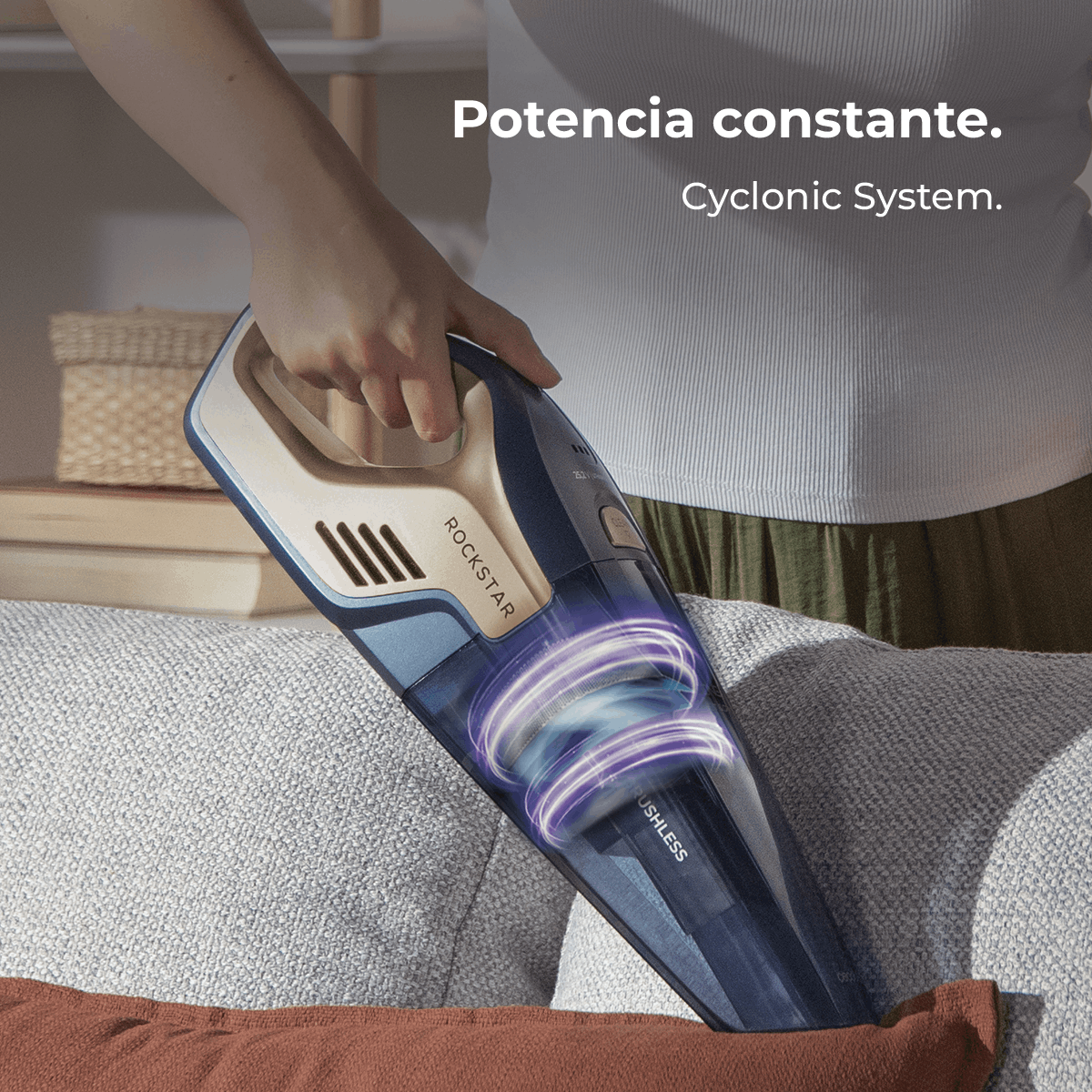 Una persona sostiene una aspiradora Rockstar azul y beige sobre un sofá gris. Las luces internas de la aspiradora giran. El texto dice 'Potencia constante'.