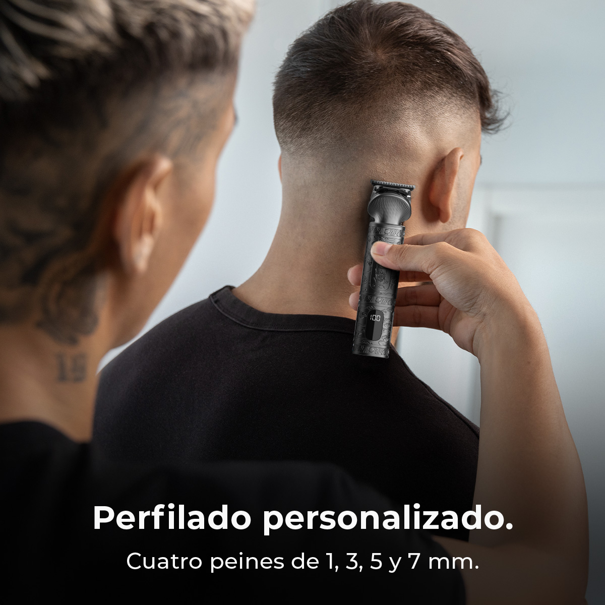 Una persona usa una recortadora en el cuello de otra, cerca de la oreja. La recortadora muestra 100 en su pantalla.