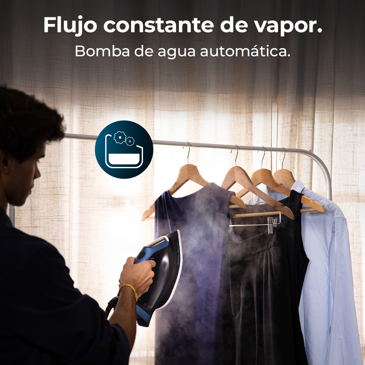 Un hombre plancha ropa con una plancha azul y negra. El vapor sale de la plancha. La ropa cuelga en una rejilla en el fondo.