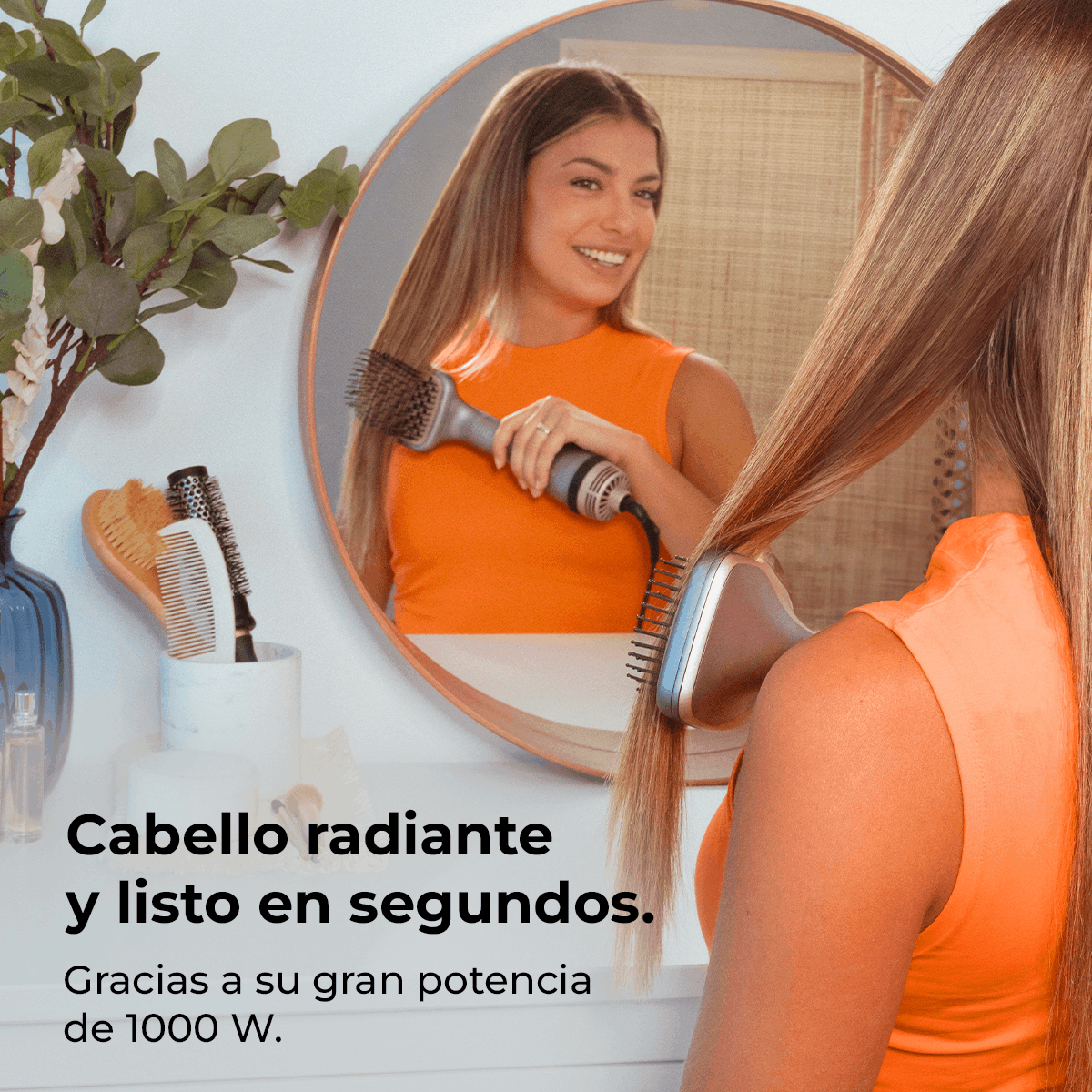 Mujer peinando su largo cabello rubio con un secador de pelo frente a un espejo, usando una camiseta naranja. Se ven otras herramientas de peinado.