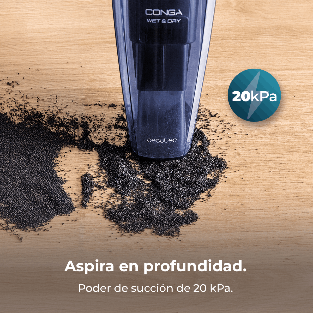Aspiradora de mano sobre madera con partículas negras dispersas. Una etiqueta muestra la potencia de succión '20kPa'.