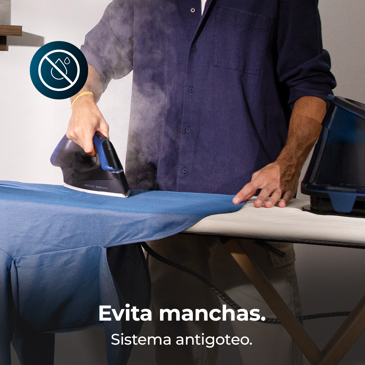 Un hombre plancha una camisa azul. El vapor sale de la plancha. Texto: 'Evita manchas. Sistema antigoteo', significa 'Evita manchas. Sistema antigoteo'.