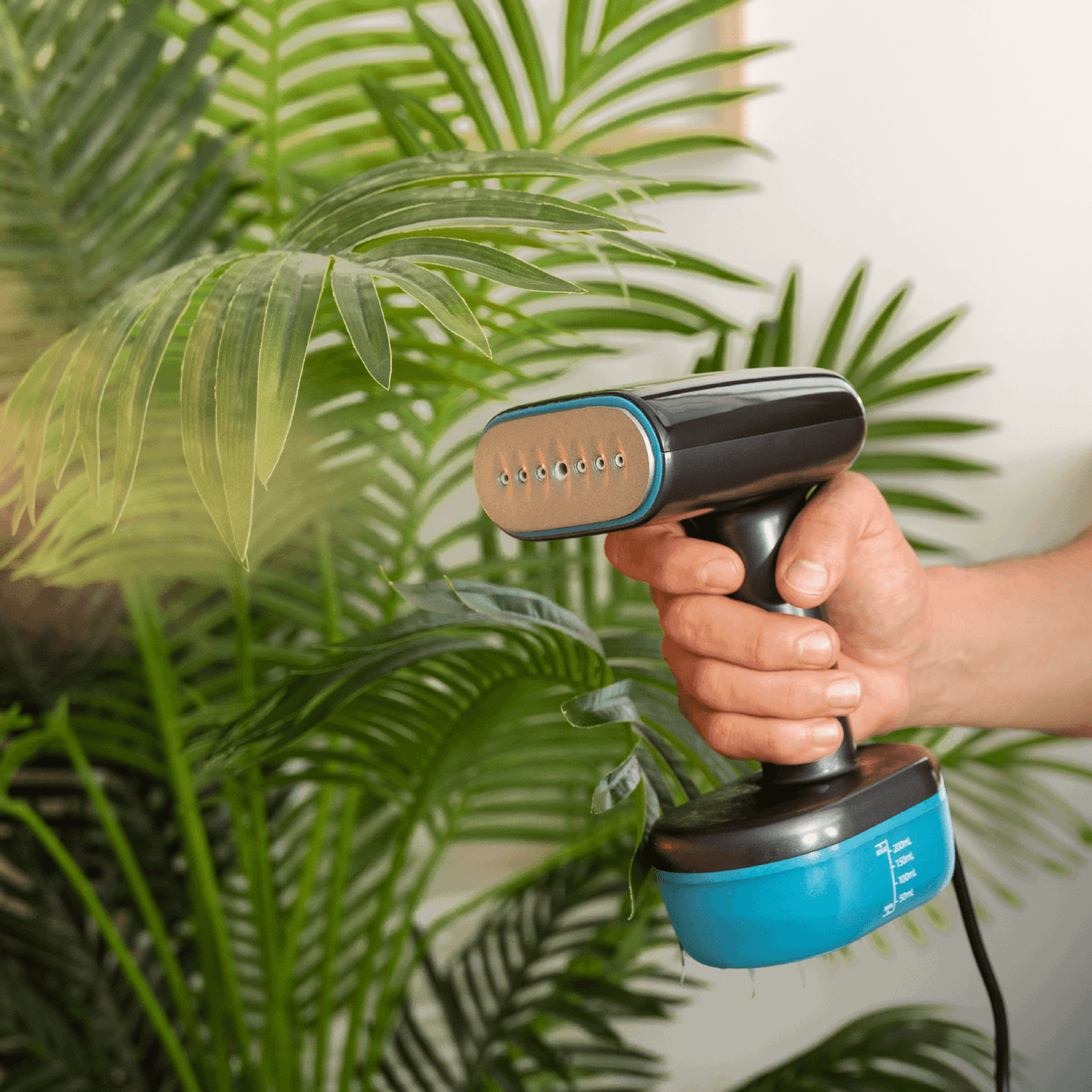 Una persona sostiene un vaporizador negro y azul cerca de hojas verdes de plantas. El vaporizador está apuntando a las hojas.