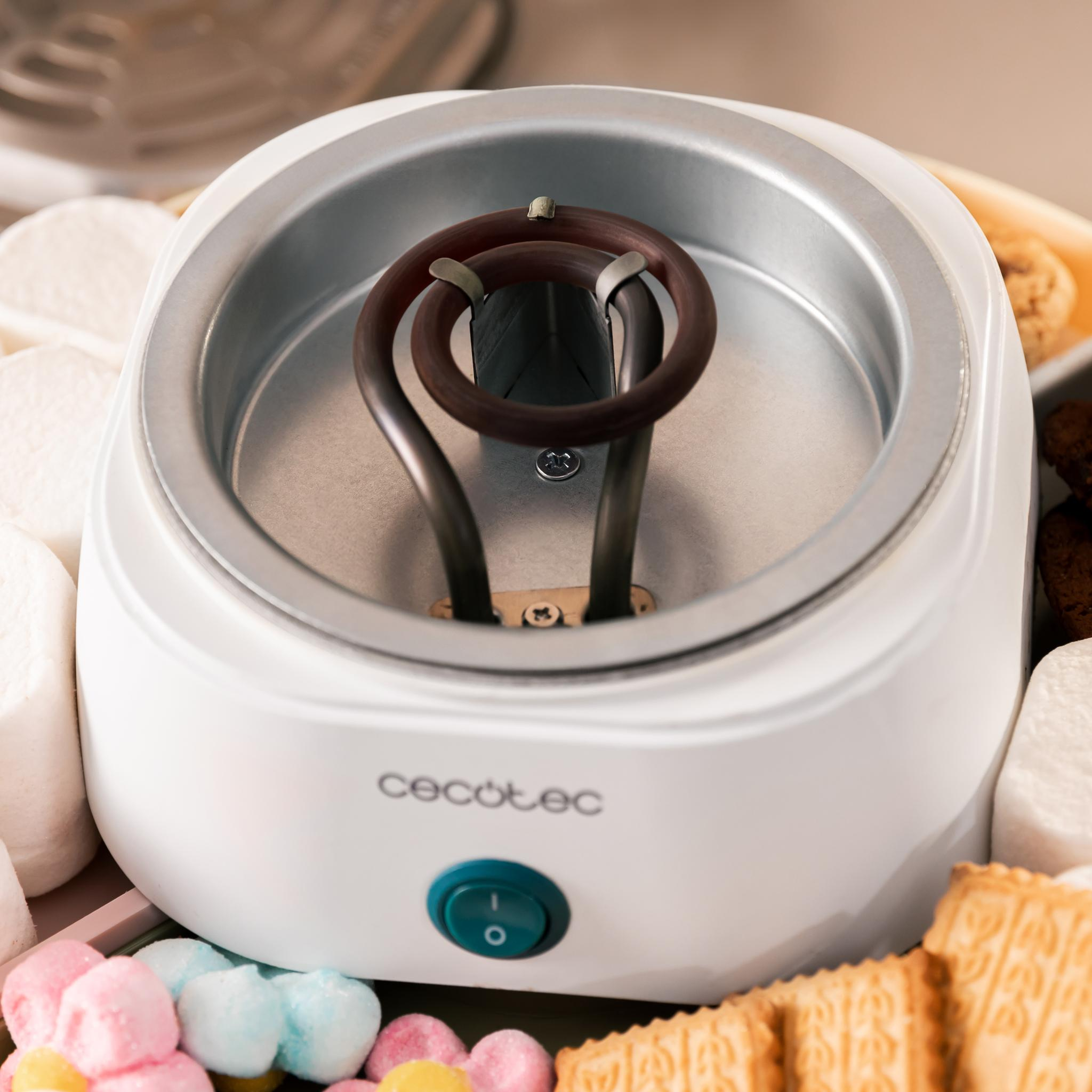 Una fondue blanca con un elemento calefactor marrón. Malvaviscos, galletas y caramelos en forma de corazón lo rodean.