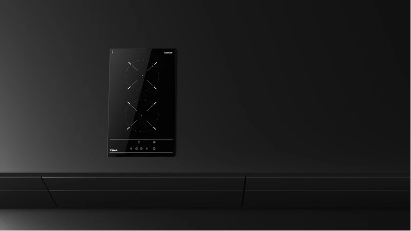 Una placa de inducción Teka negra está sobre una superficie negra. Tiene dos quemadores con marcas blancas. El fondo es negro.