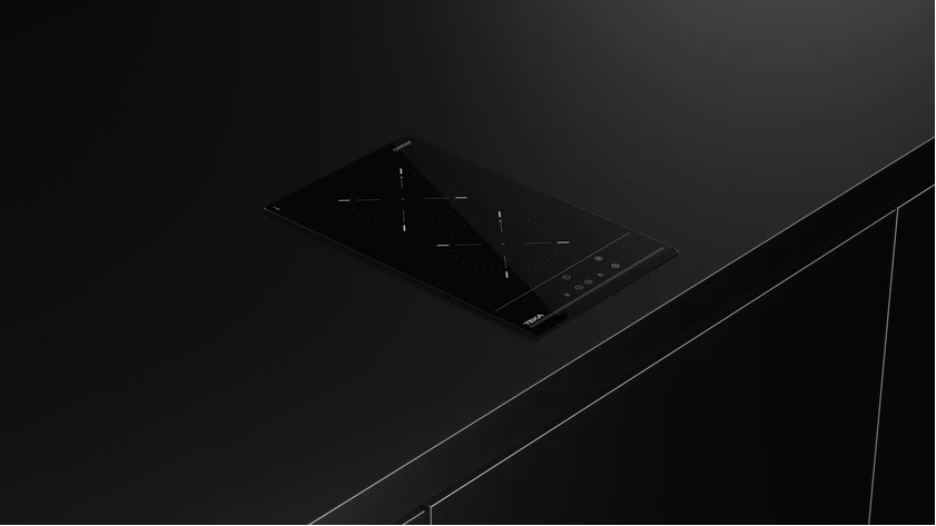 Una placa de inducción Teka negra sobre una superficie oscura. Cuenta con cuatro zonas de cocción y panel de control.