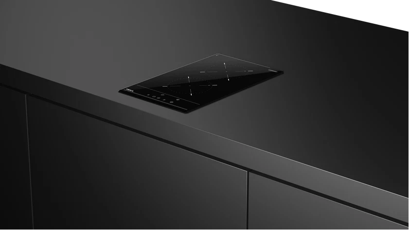 Una moderna placa de inducción negra está empotrada en una encimera gris oscura. Debajo, un armario gris oscuro.