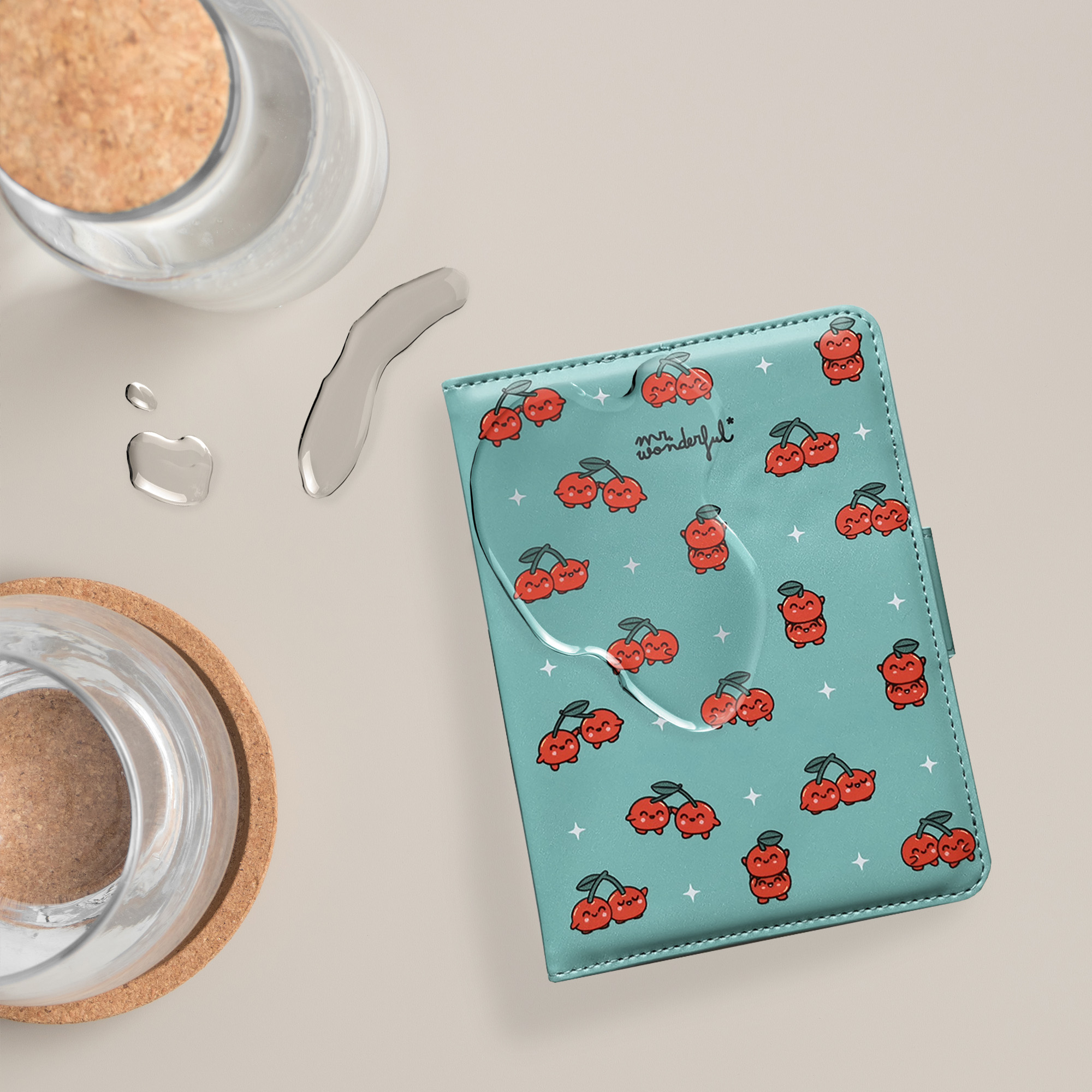 Un cuaderno turquesa con diseños de cerezas, gotas de agua y frascos de vidrio sobre una superficie beige.