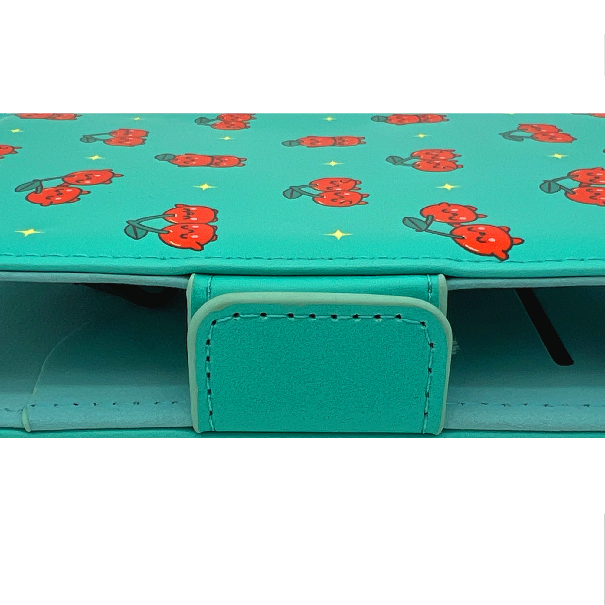 Una funda turquesa con un patrón de cerezas rojas. Se ve un cierre turquesa. Fondo blanco.