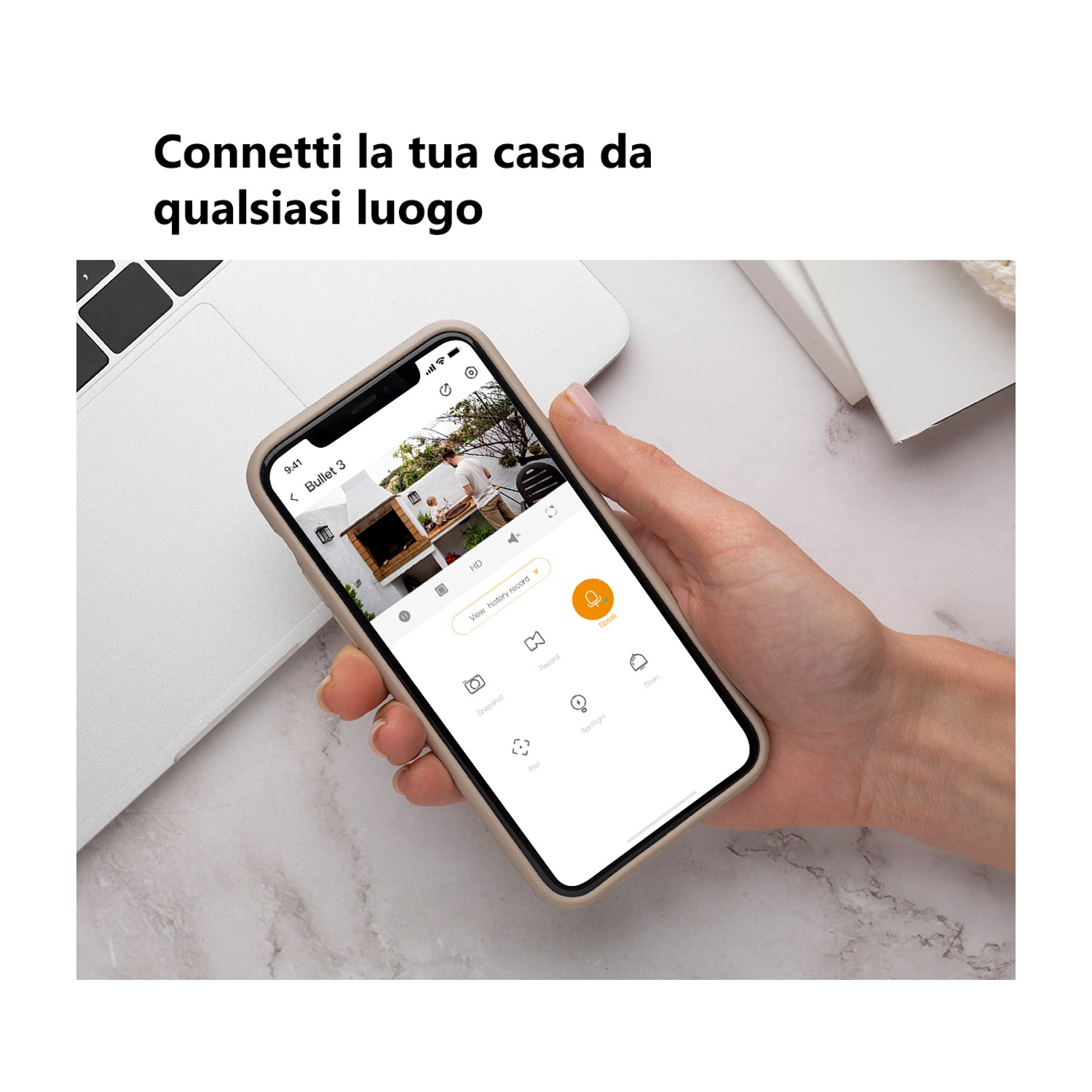 Una mano tiene uno smartphone che mostra l'interfaccia di un'app di sicurezza domestica. Il telefono mostra un live feed.