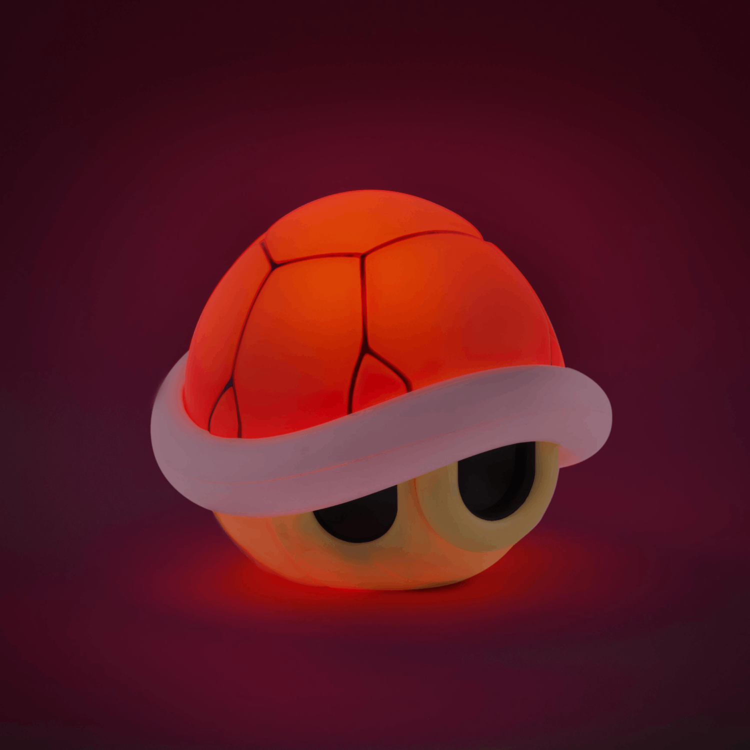 Una concha de Koopa iluminada. La concha es naranja, blanca y amarilla. Tiene agujeros negros para los ojos sobre un fondo rojo oscuro.