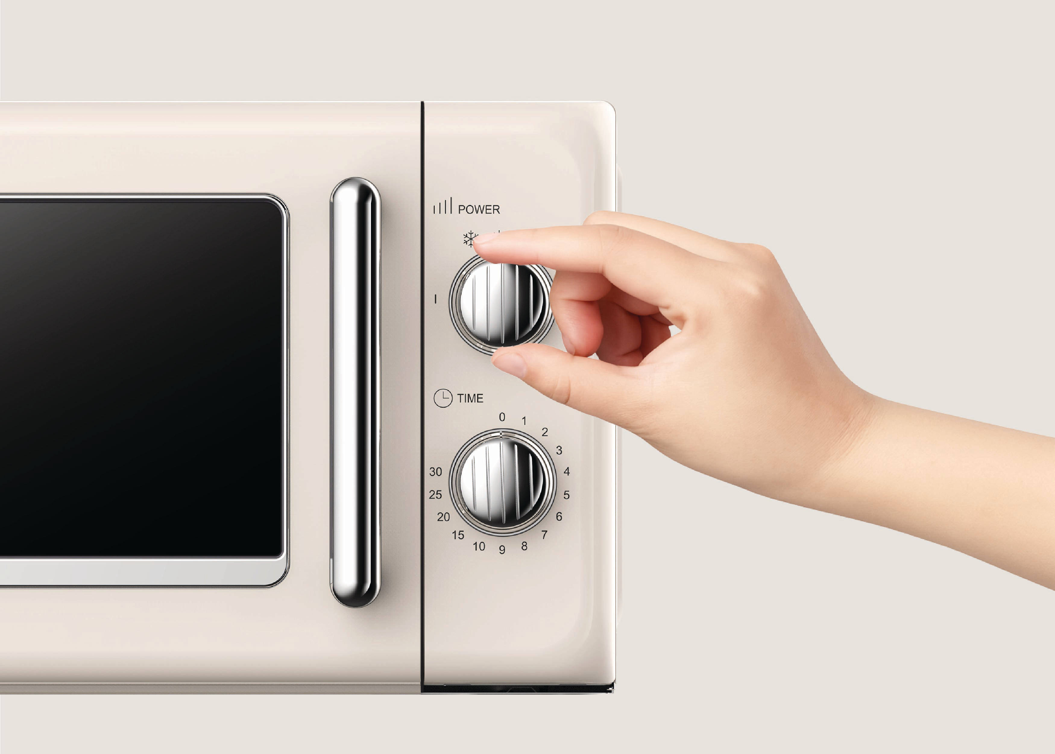 Eine Hand dreht den Leistungsregler der Mikrowelle. Beige Mikrowelle mit schwarzer Tür. Das Leistungsrad hat ein Schneeflockensymbol.
