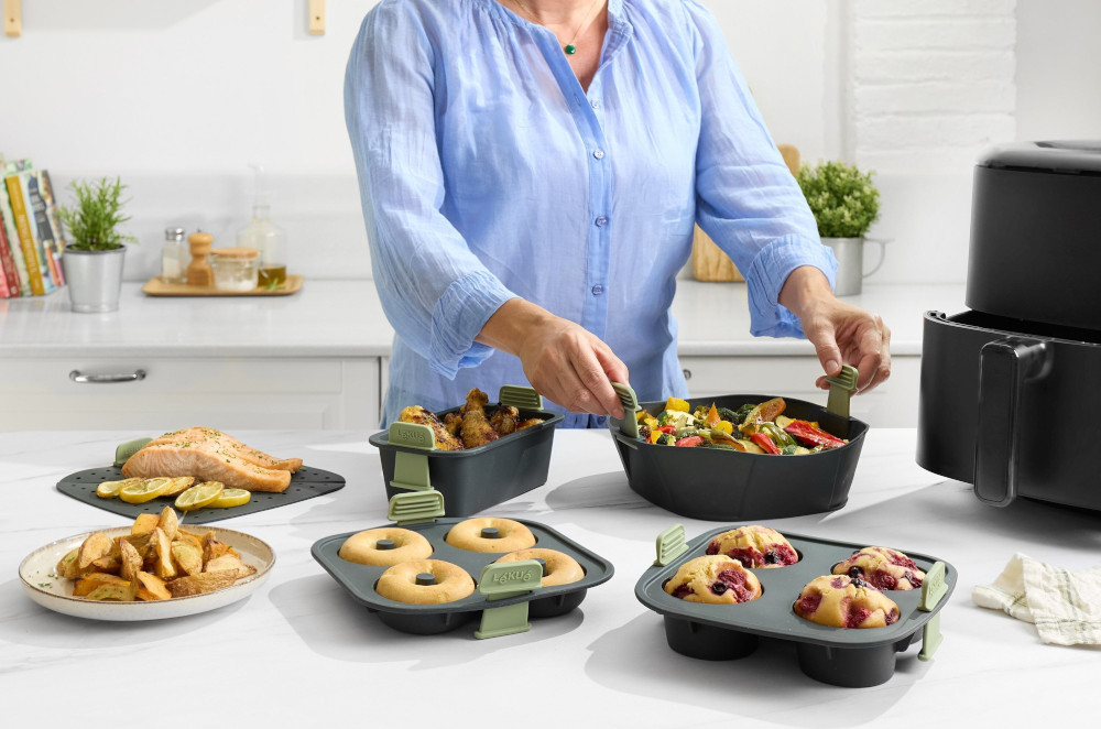 A person in a blue shirt prepares food. There is salmon, donuts, muffins, and vegetables. An air fryer is in the background.