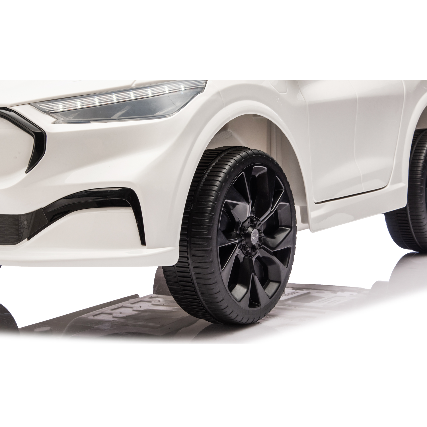 Close-up of a white toy car. Black tires and rims are visible. The car is on a reflective surface. Headlight detail is also shown.