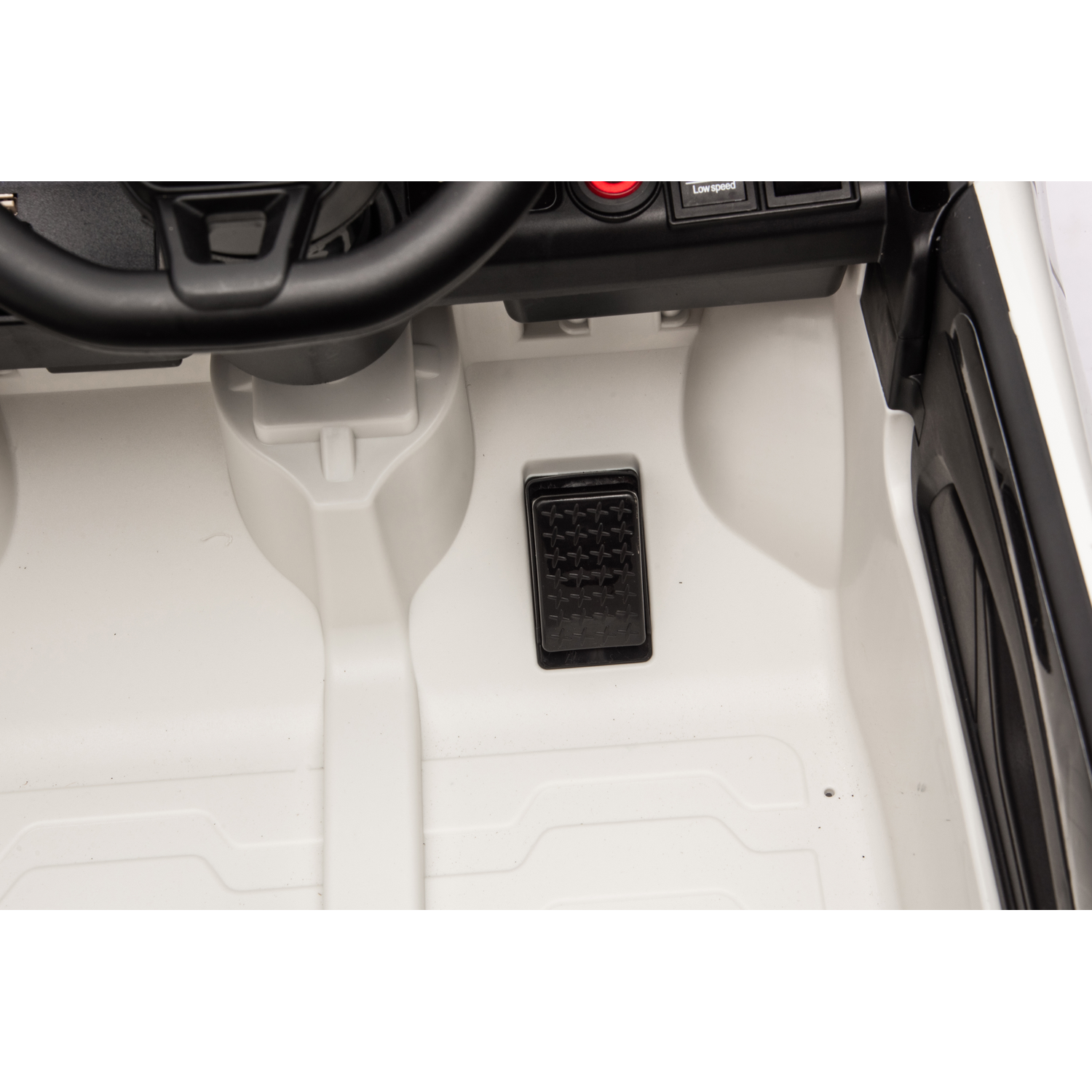 Inside a toy car: steering wheel, dashboard, pedal, and white interior. Low speed button is visible.