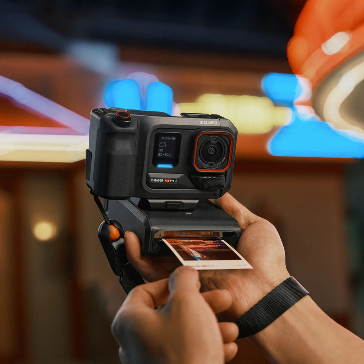 Una persona tiene in mano una fotocamera nera Insta360 Ace Pro 2, che produce una foto. La fotocamera è nera con un anello arancione.