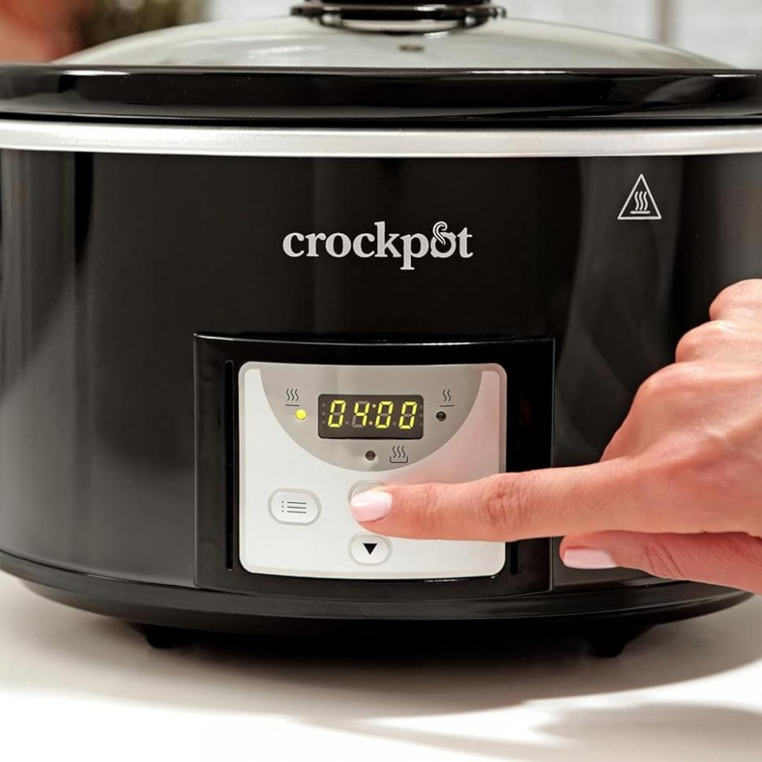 A black Crock-Pot with a digital display showing 0:00. A hand is pressing a button on the control panel.