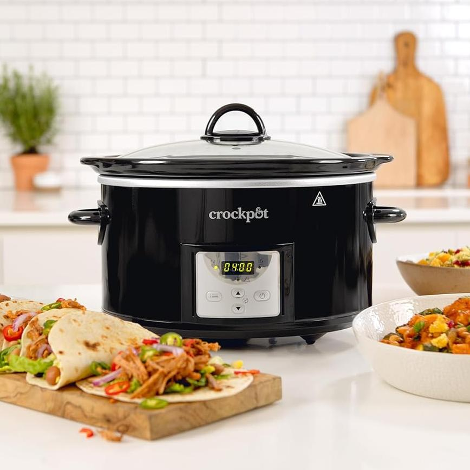 Black Crock-Pot with tacos and side dishes on a white countertop. A cutting board with tacos in the foreground.