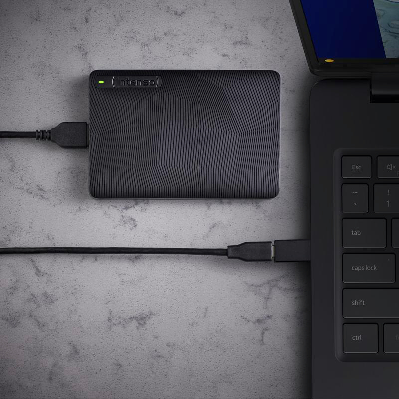 Schwarze externe Festplatte, verbunden mit einem Laptop über USB-Kabel auf strukturierter Oberfläche. Die Festplatte ist von Intenso.