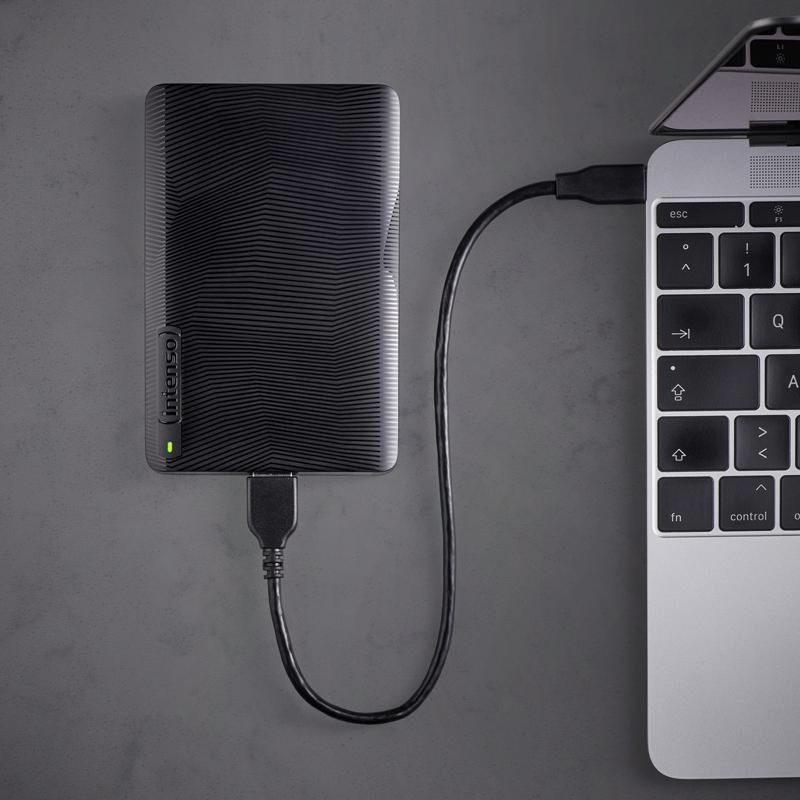 Eine schwarze externe Festplatte ist mit einem MacBook mit einem schwarzen USB-Kabel auf einer grauen Oberfläche verbunden.
