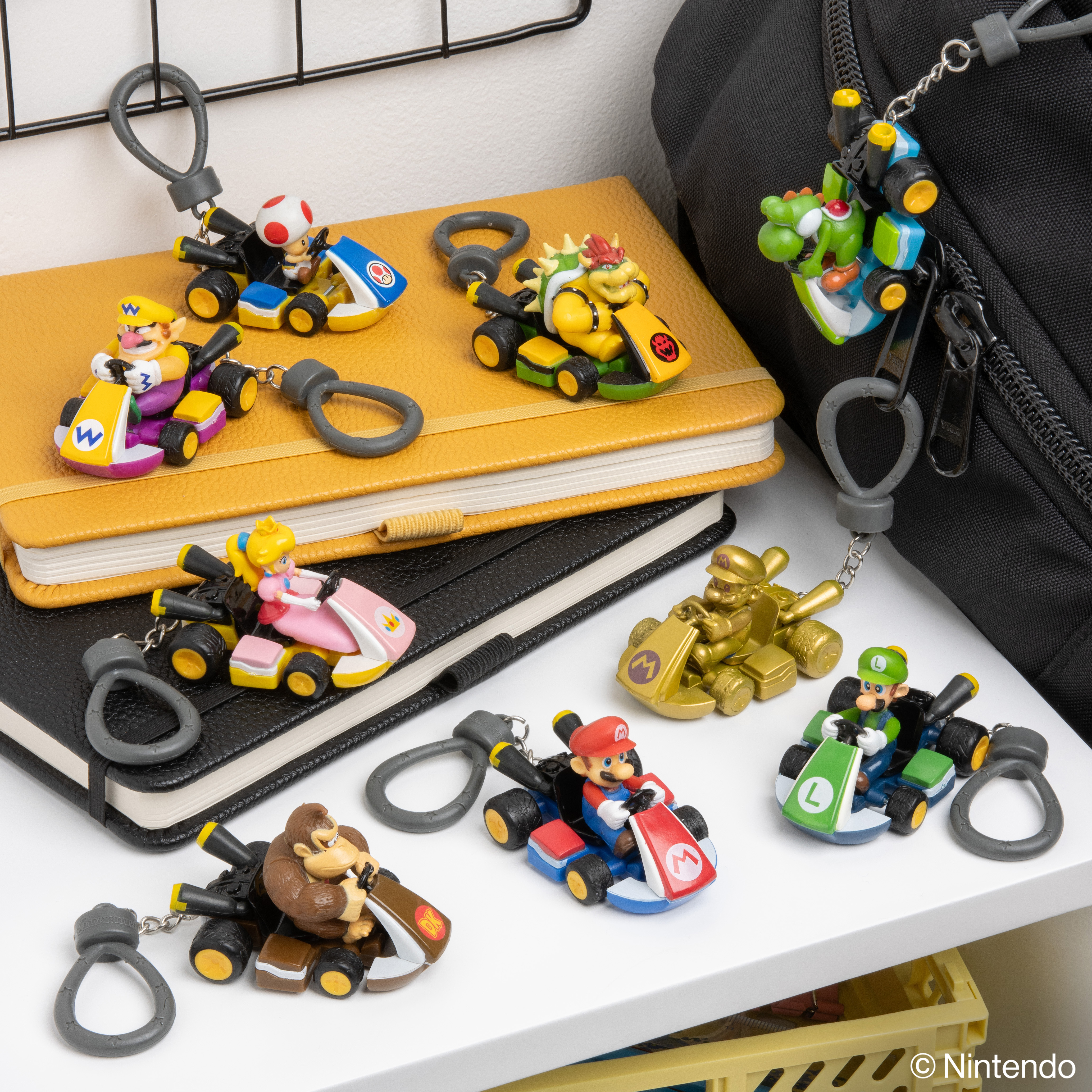 Schlüsselanhänger von Mario Kart-Charakteren auf Notizbüchern, einer Tasche und einem Regal. Charaktere sind Mario, Luigi und Bowser.