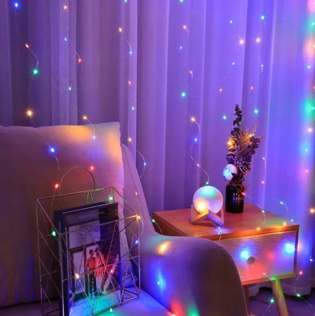 Pokój z lampkami choinkowymi, sofą, stolikiem nocnym z lampą i wazonem oraz złotym stojakiem na czasopisma.