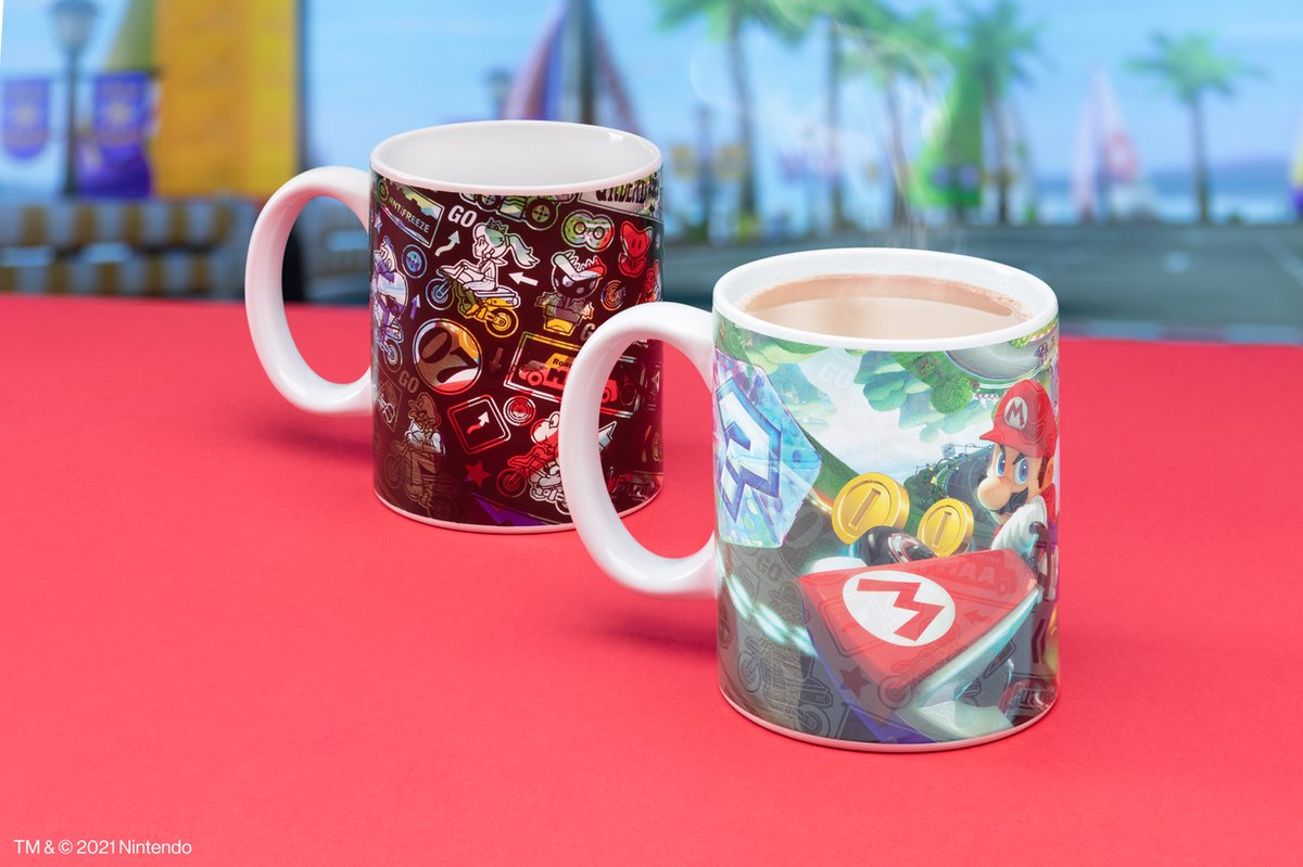 Dos tazas de Mario en una superficie roja. Una tiene personajes de Mario, la otra imágenes de Mario Kart con Mario y monedas.