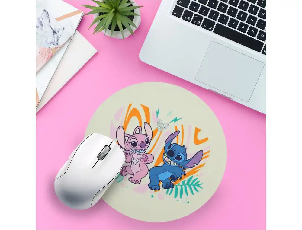 Un ratón blanco está en un escritorio rosa junto a una alfombrilla con Stitch y Angel. También se ven un portátil y una planta.